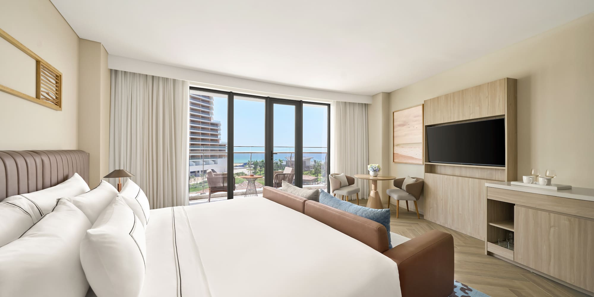 Modern luxury hotel room with ocean view balcony, large bed, and sofa.