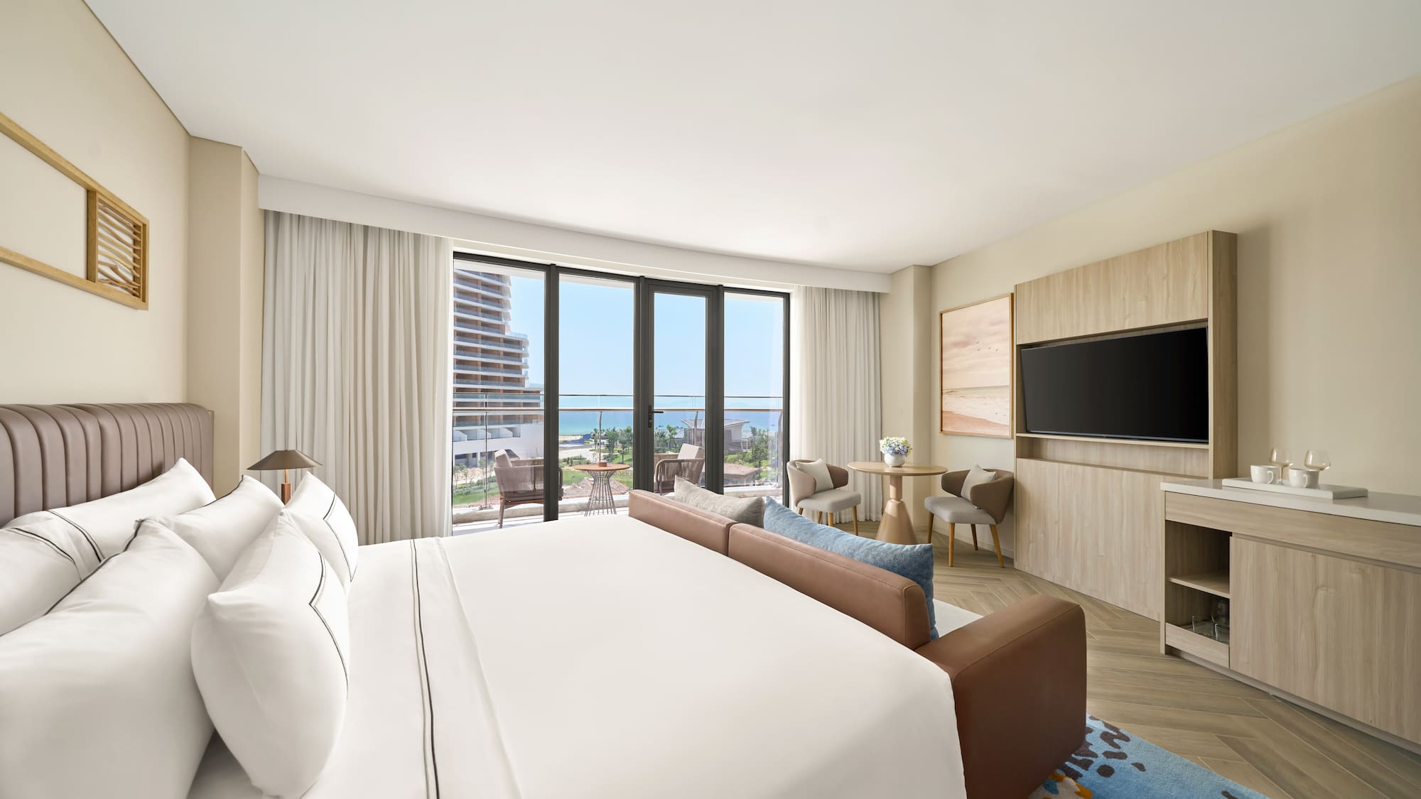Modern luxury hotel room with ocean view balcony, large bed, and sofa.