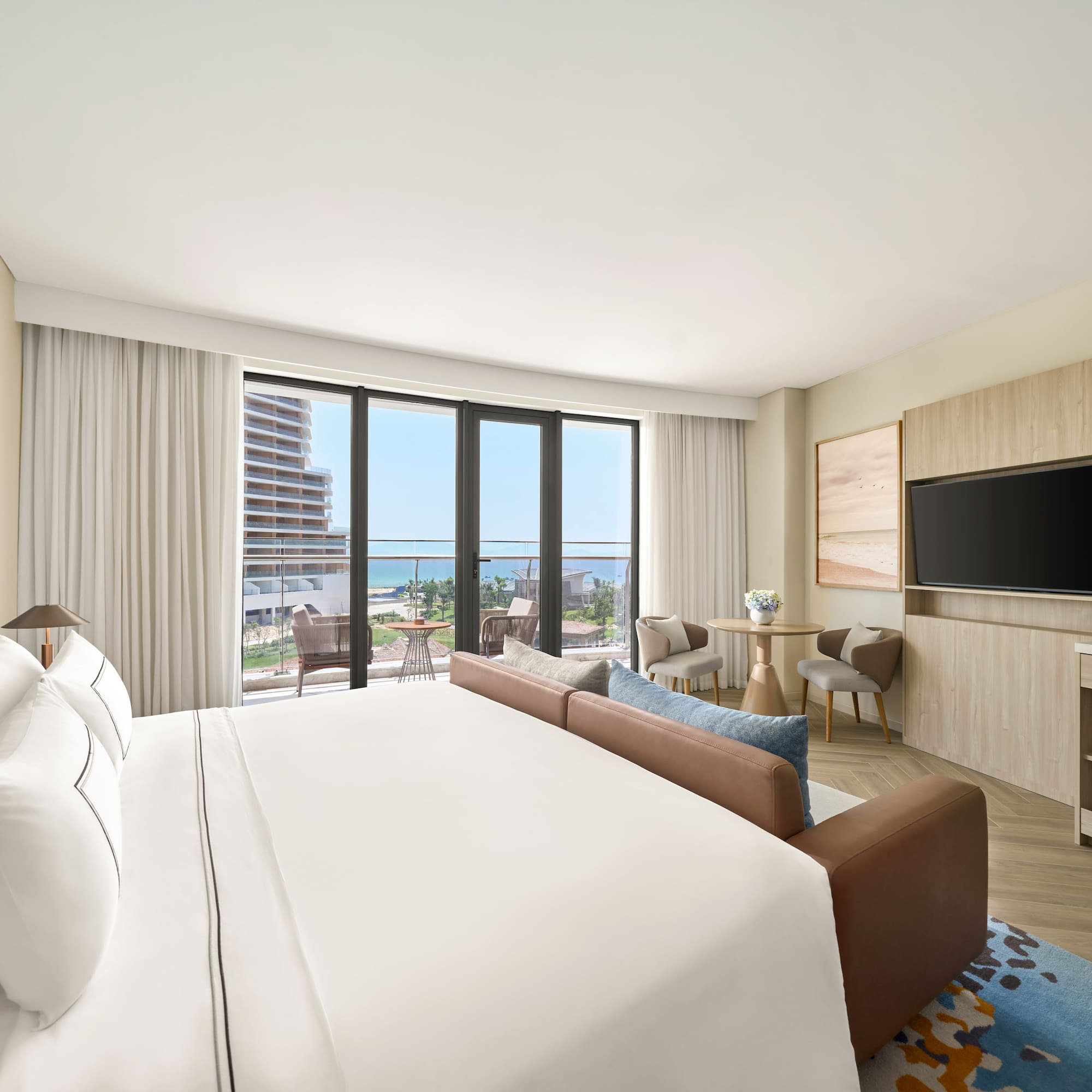 Modern luxury hotel room with ocean view balcony, large bed, and sofa.