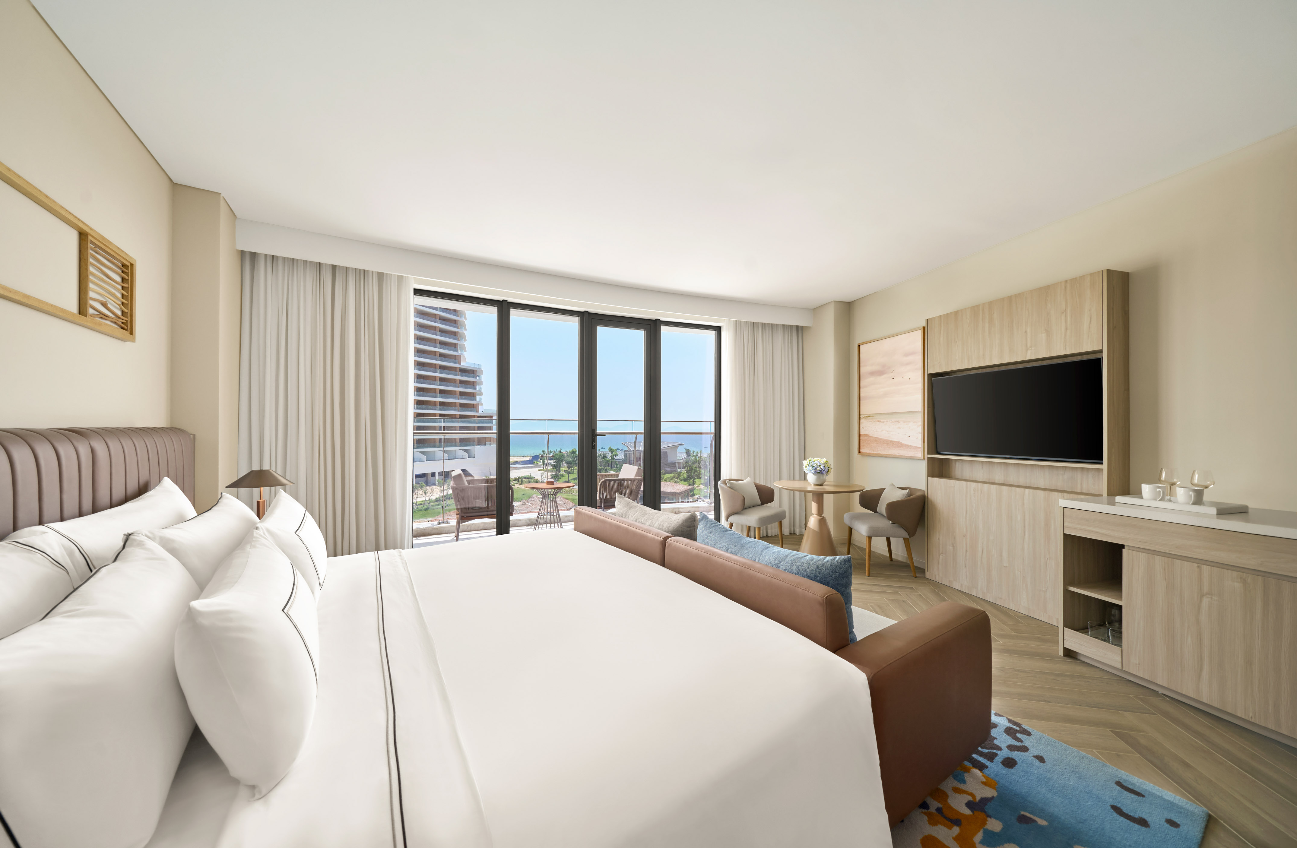 Modern luxury hotel room with ocean view balcony, large bed, and sofa.