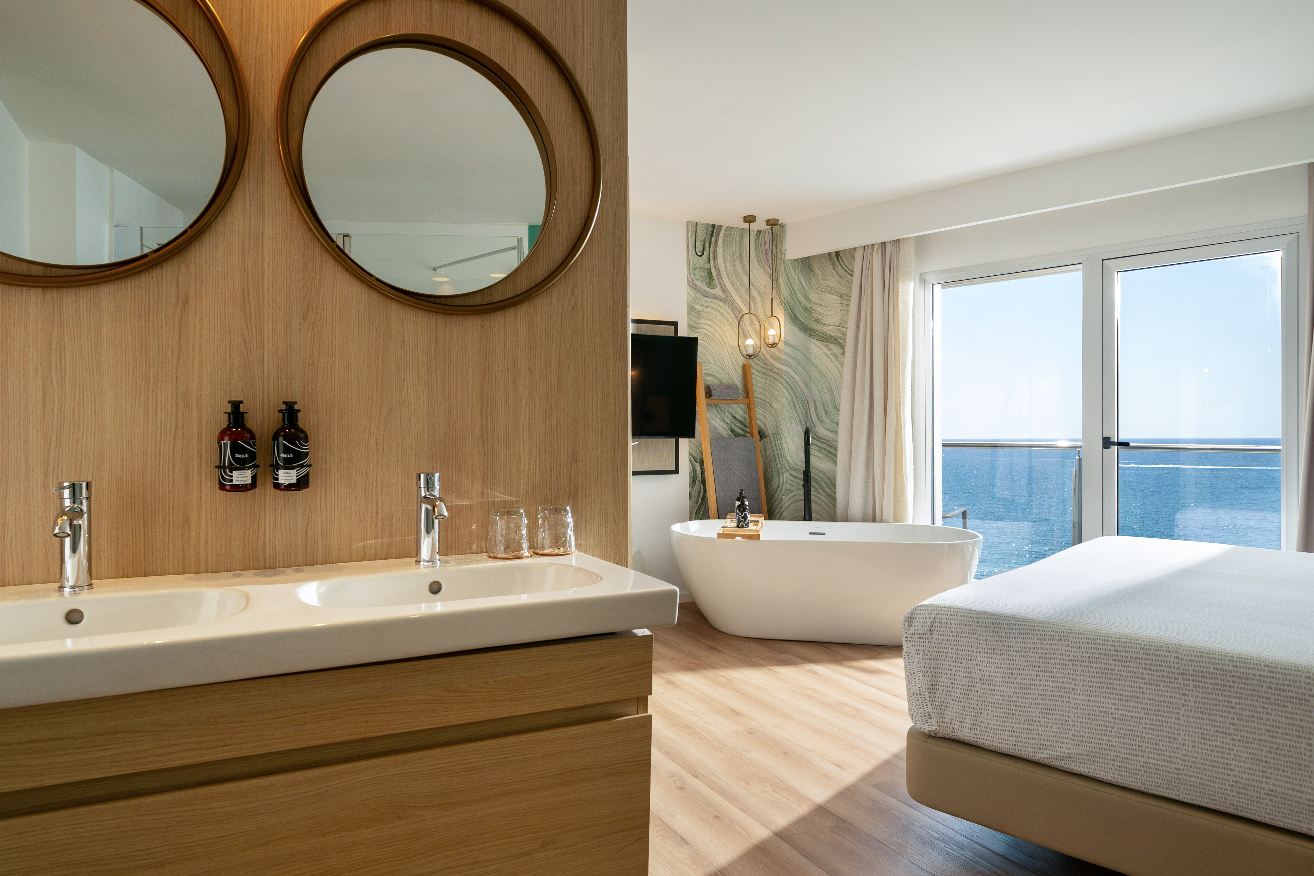 Ocean view modern hotel room with double sinks and freestanding tub.