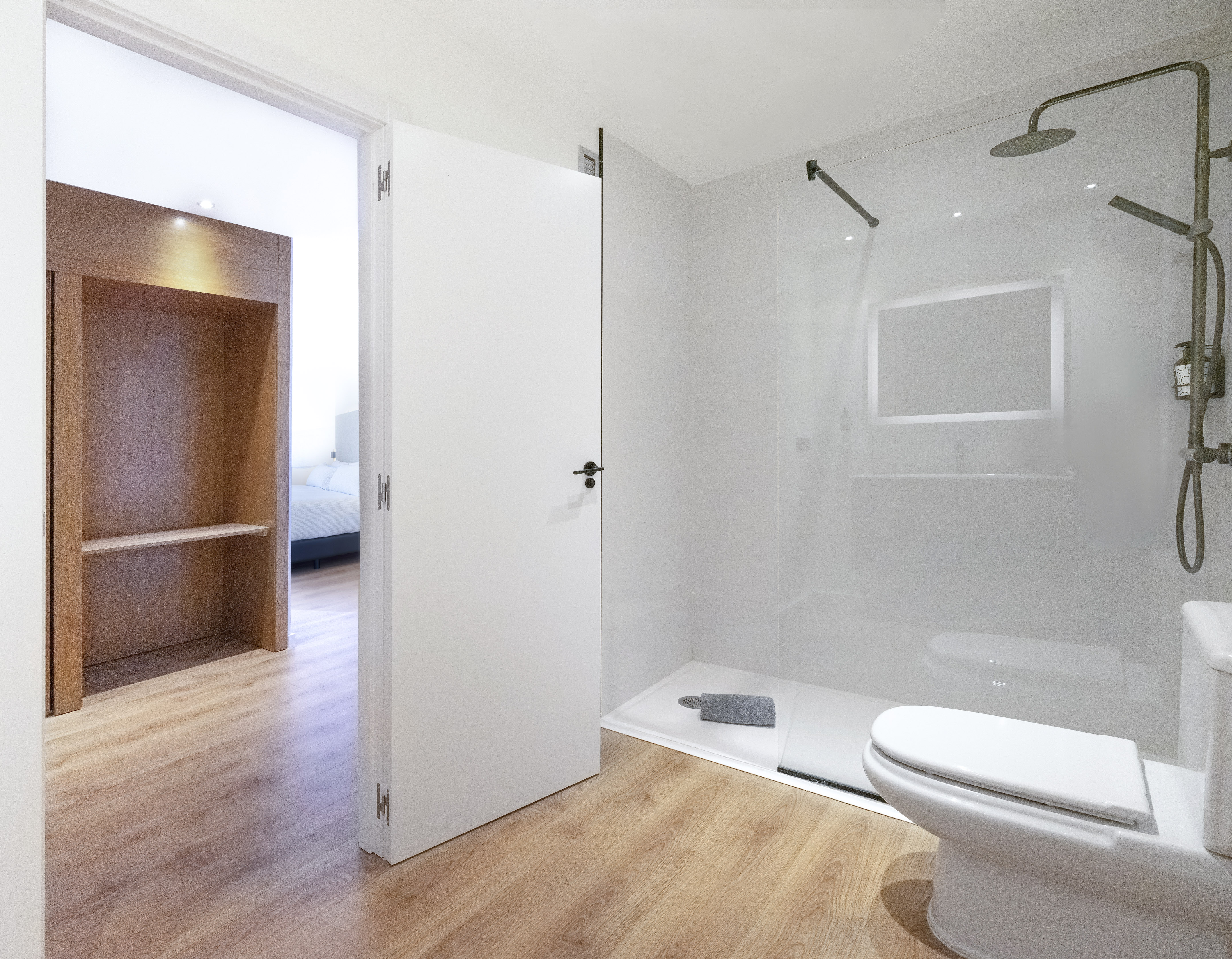 Modern bathroom with glass shower, toilet, and doorway to light-filled bedroom.