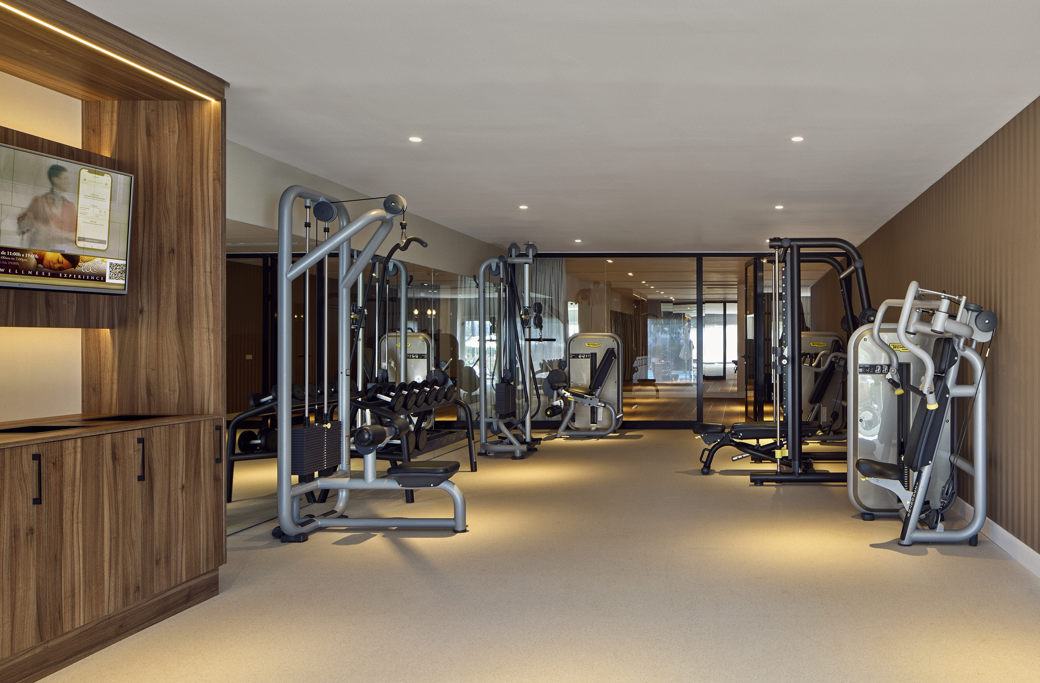 Modern gym with various exercise machines, free weights, and wellness TV.