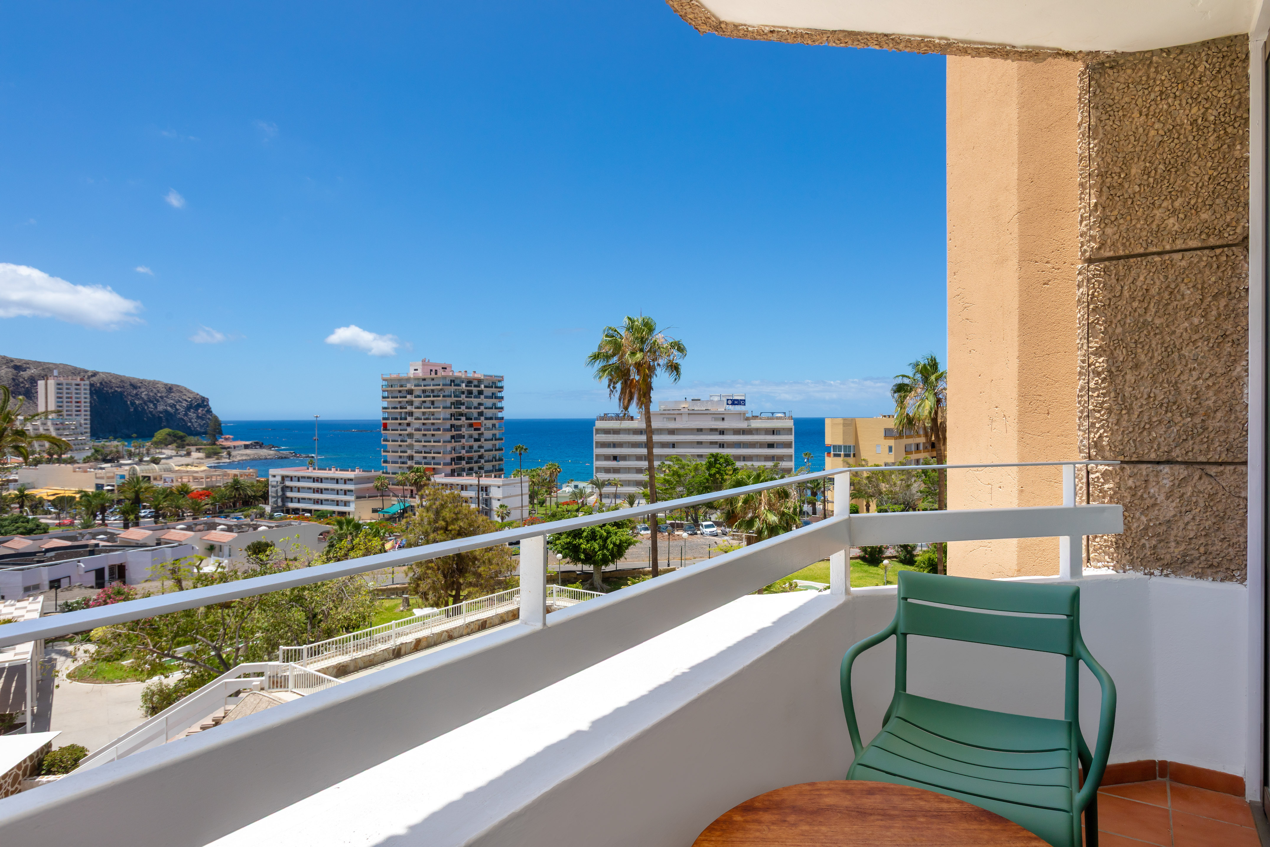 Coastal balcony with sea view, buildings, and palm trees.