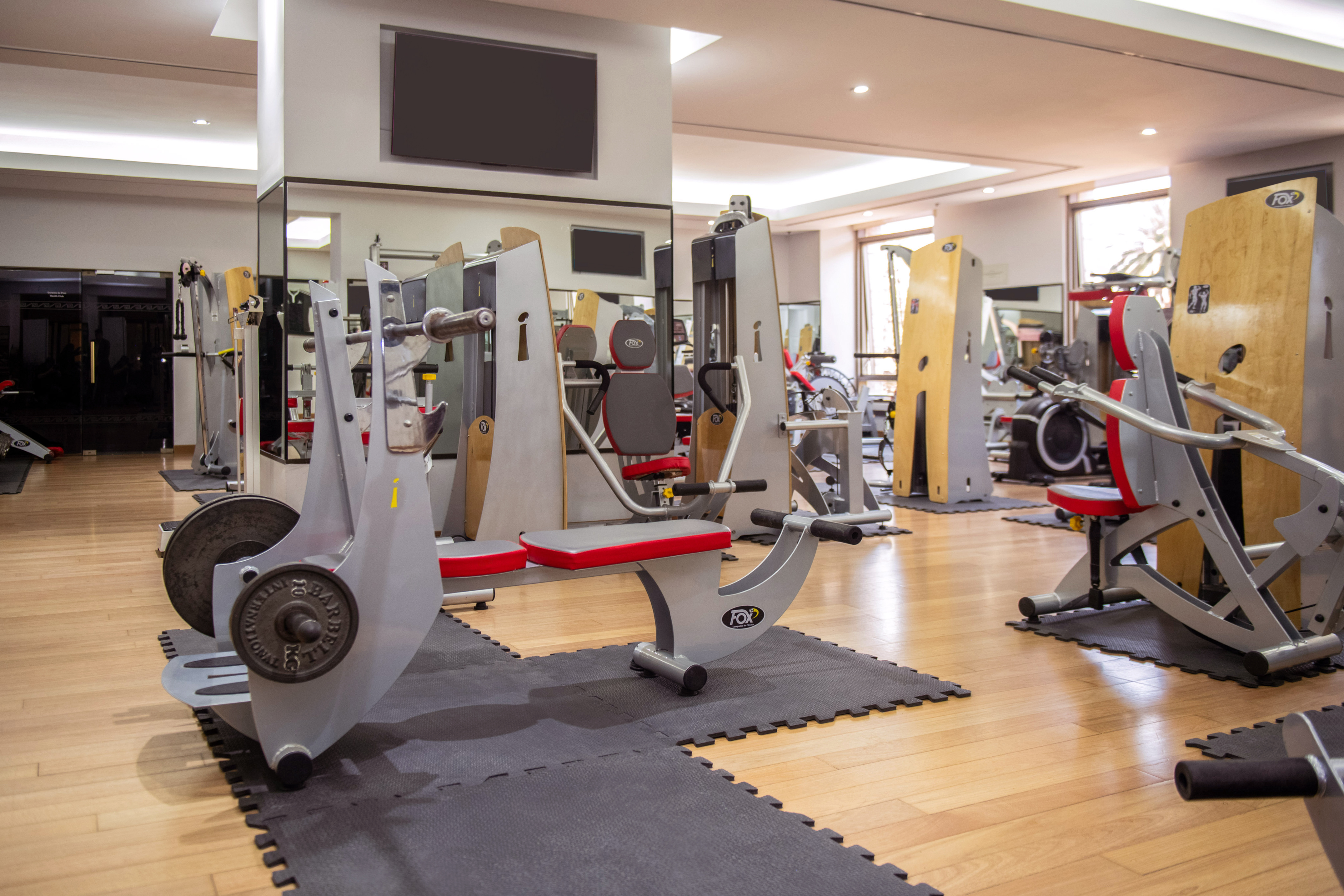 Well-equipped gym with weight machines, benches, and light wooden flooring.