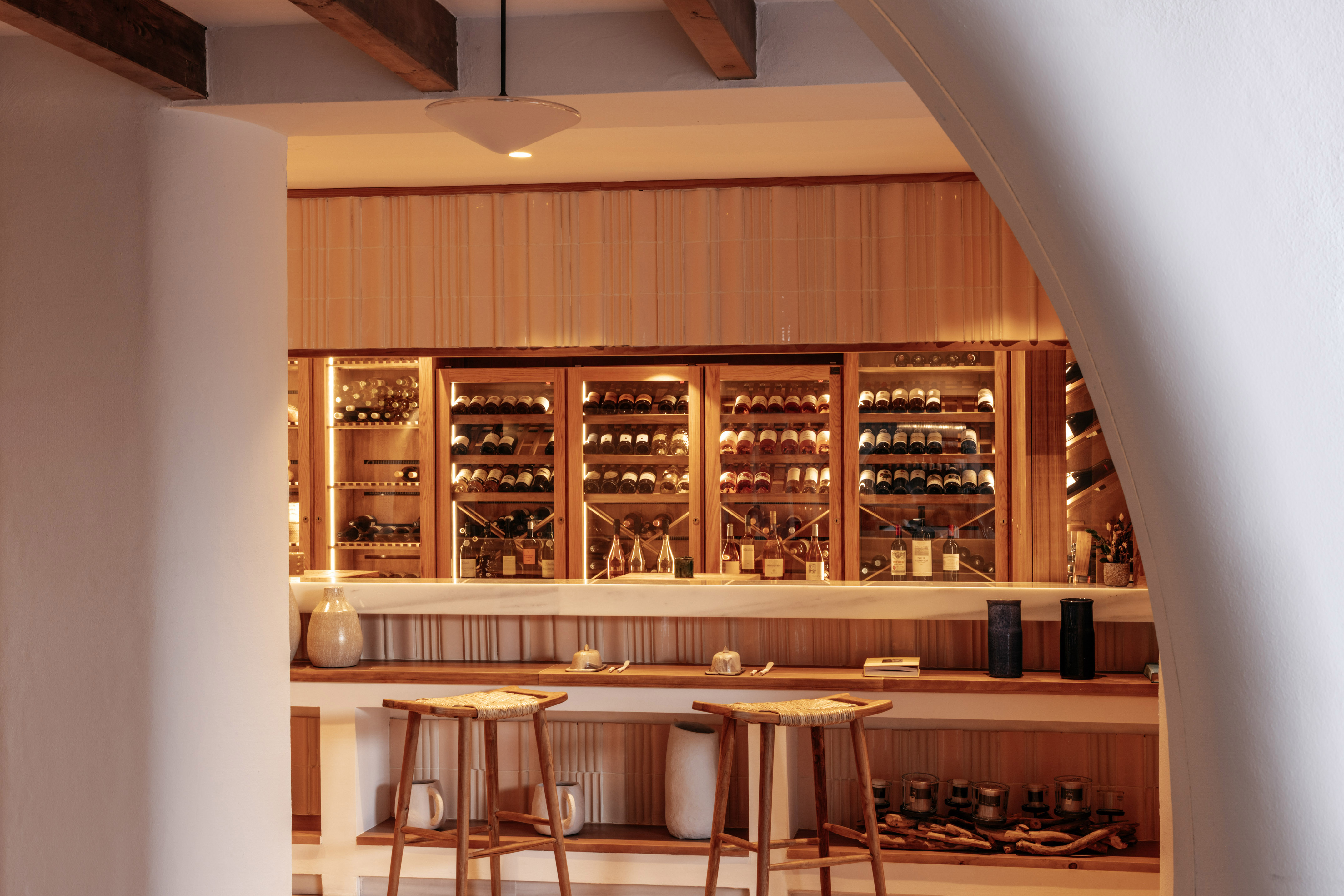 Modern wine display bar with illuminated cabinets and wooden stools.