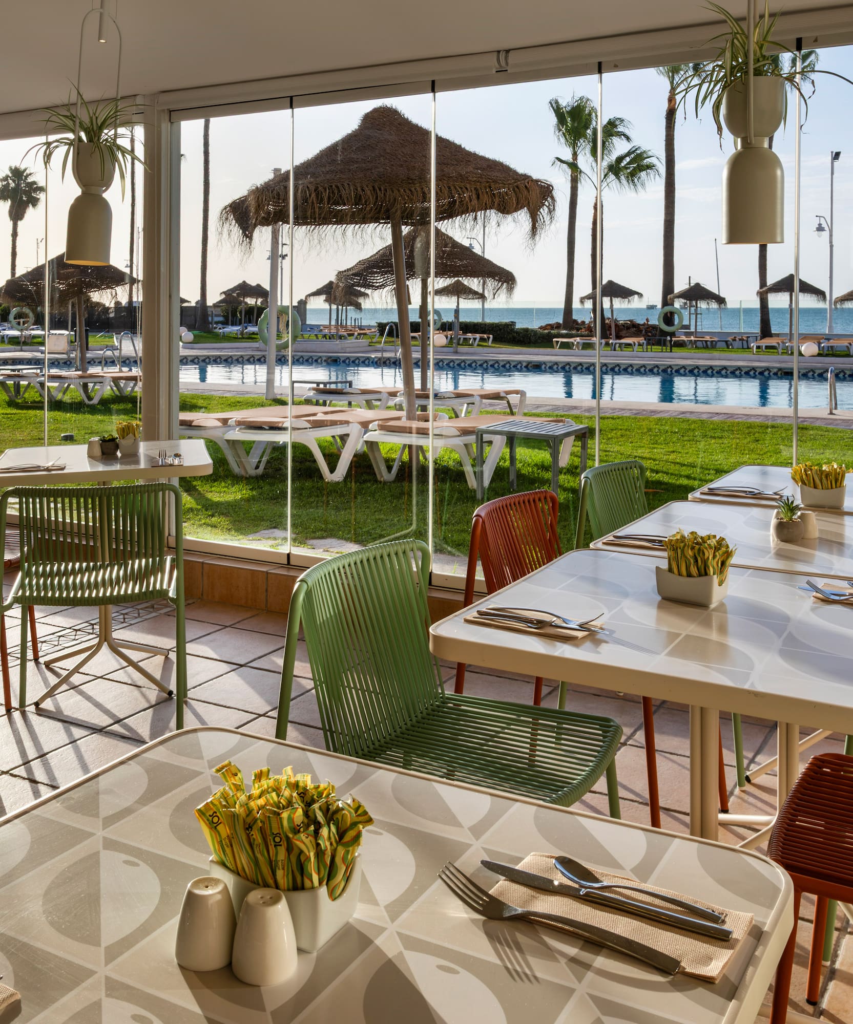Restaurant patio overlooking a pool, palm trees, and ocean beach.