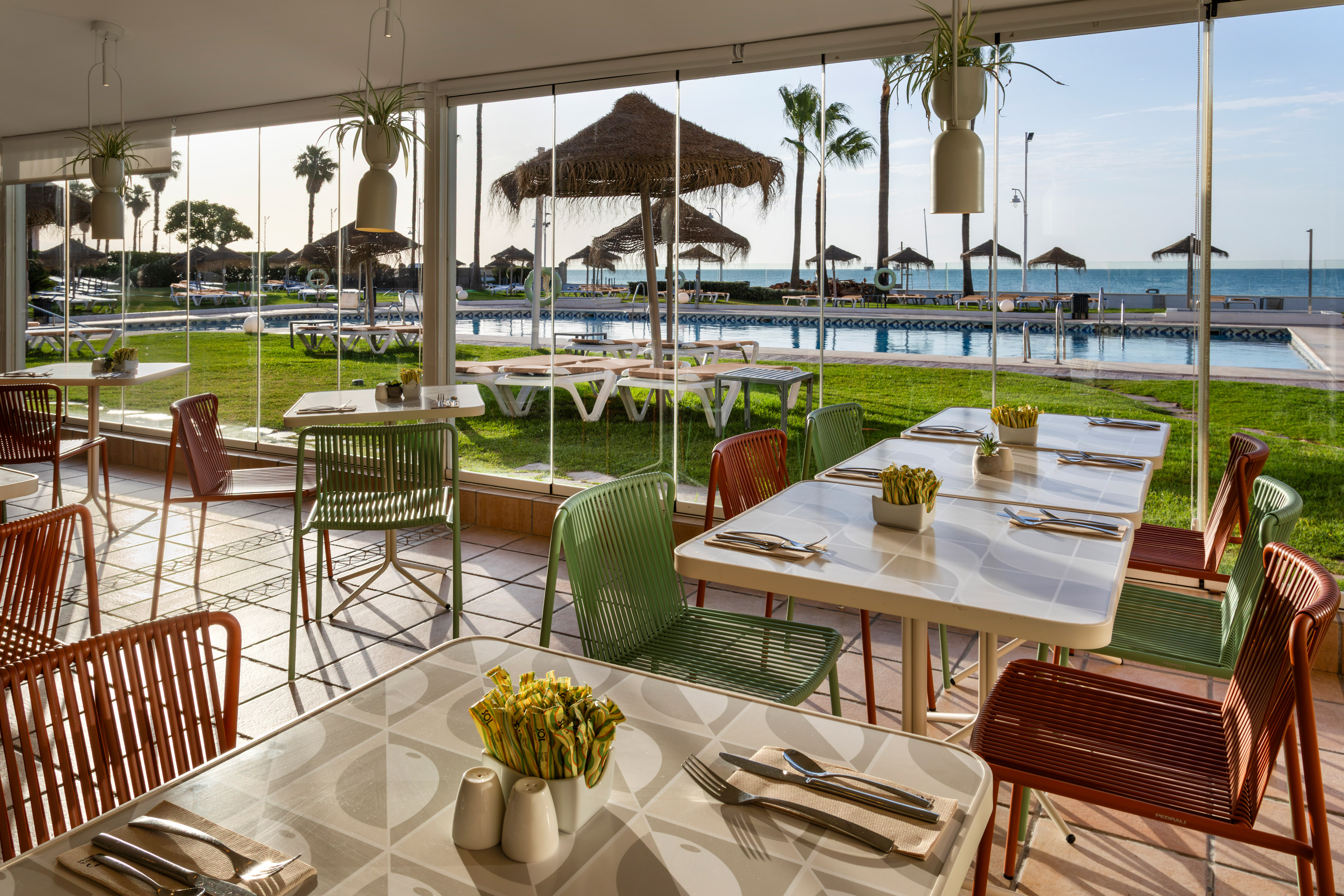 Restaurant patio overlooking a pool, palm trees, and ocean beach.