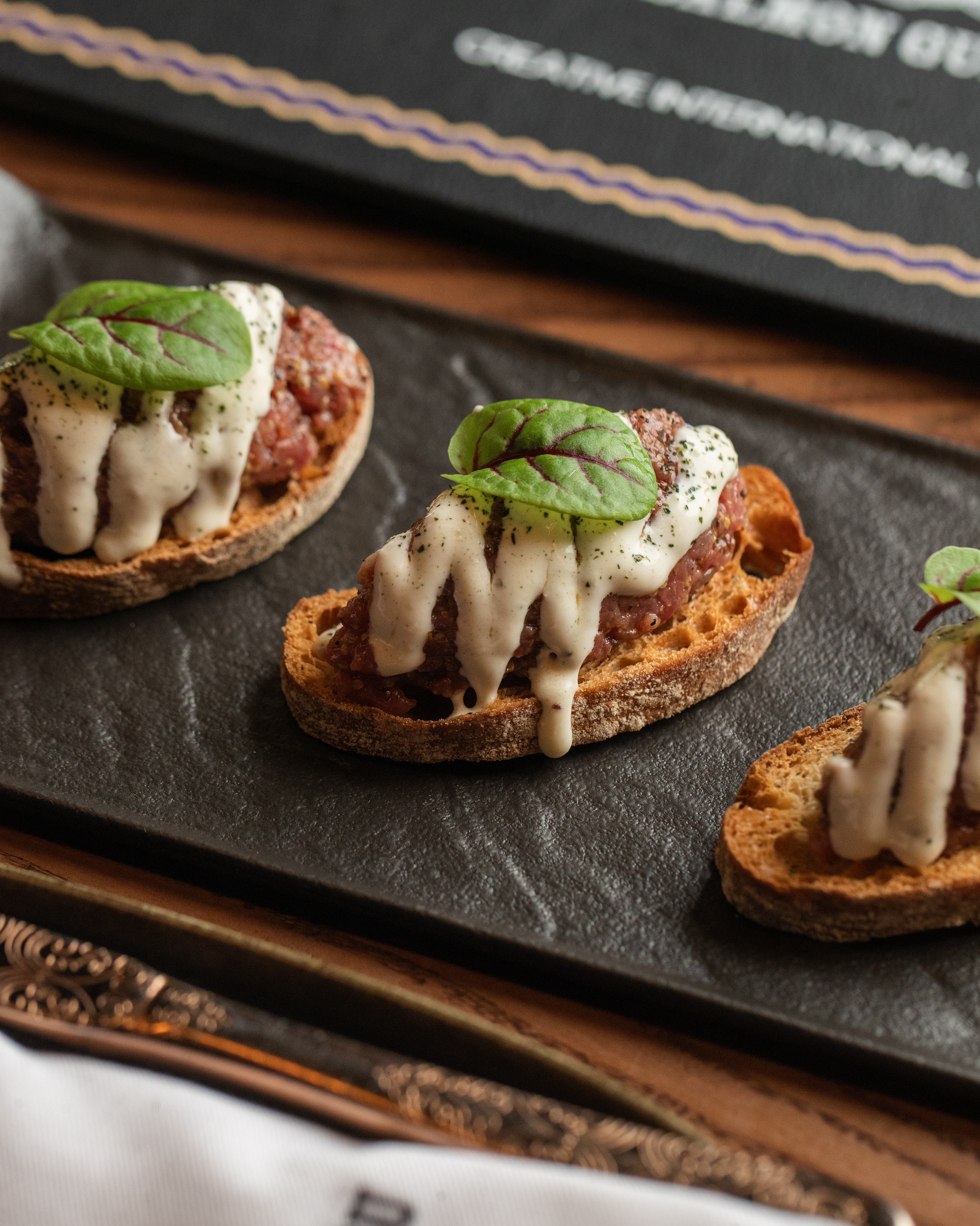 Gourmet beef tartare canapés on crostini with creamy sauce and greens.