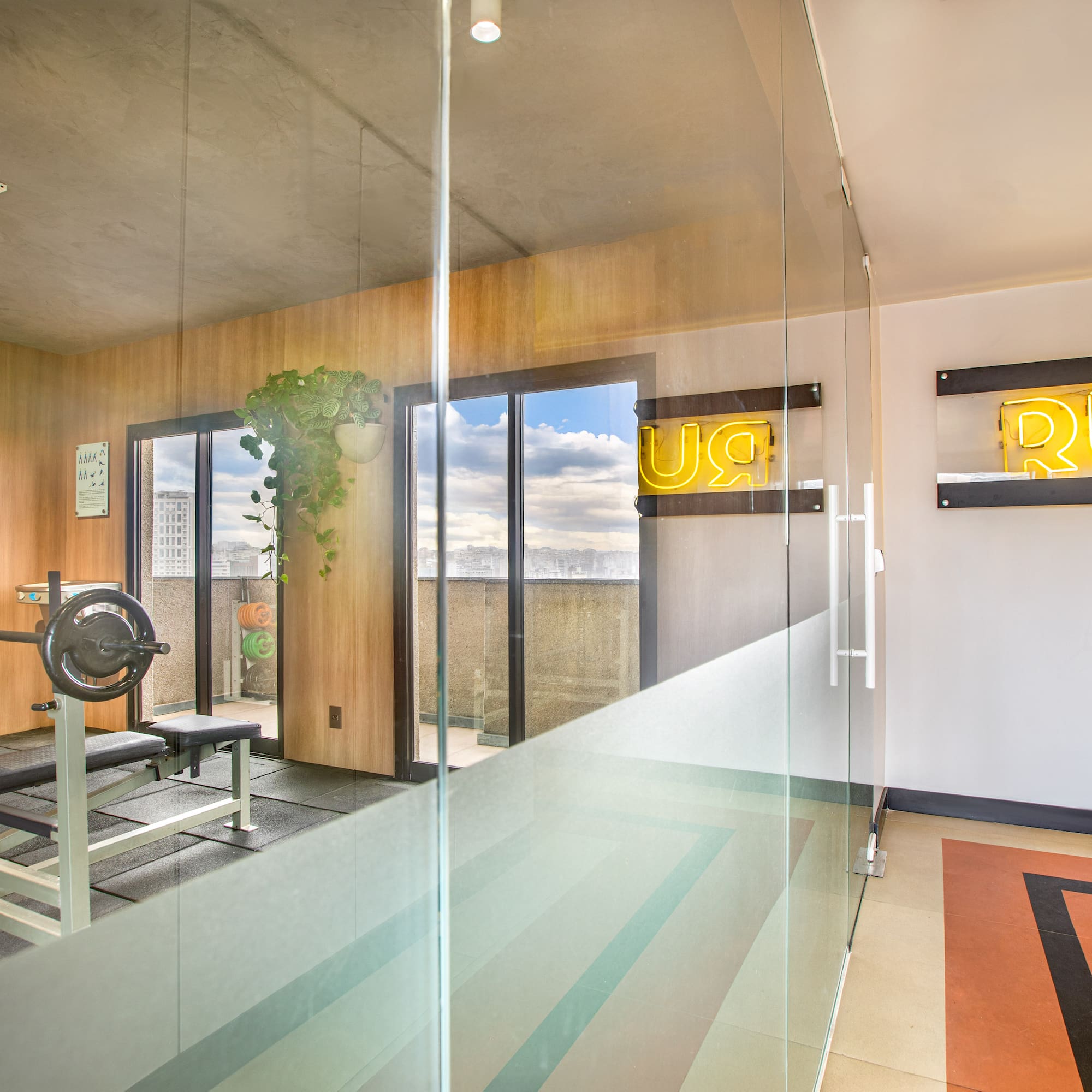 Modern home gym with bench press, weights, "RUN" neon sign, and city view.