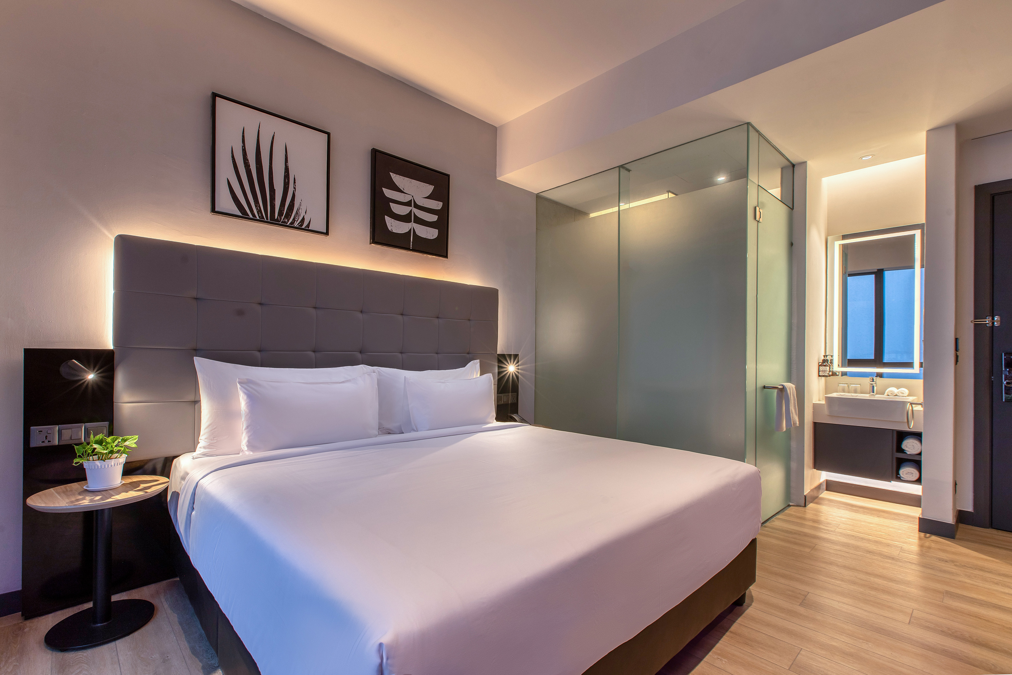 Modern hotel room with king bed, backlit headboard, and glass-partitioned bathroom.