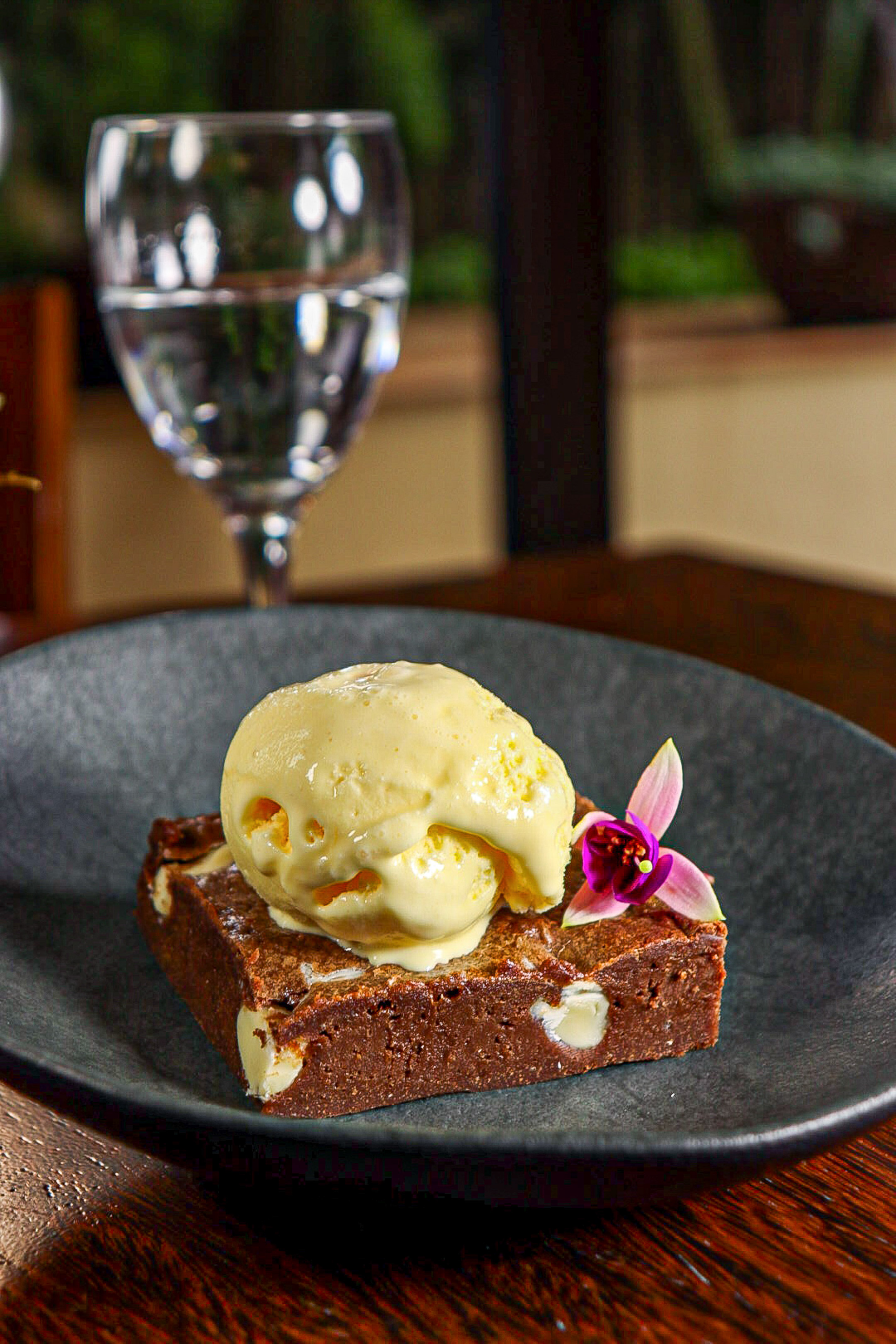 White chocolate chip brownie topped with vanilla ice cream and pink flower.