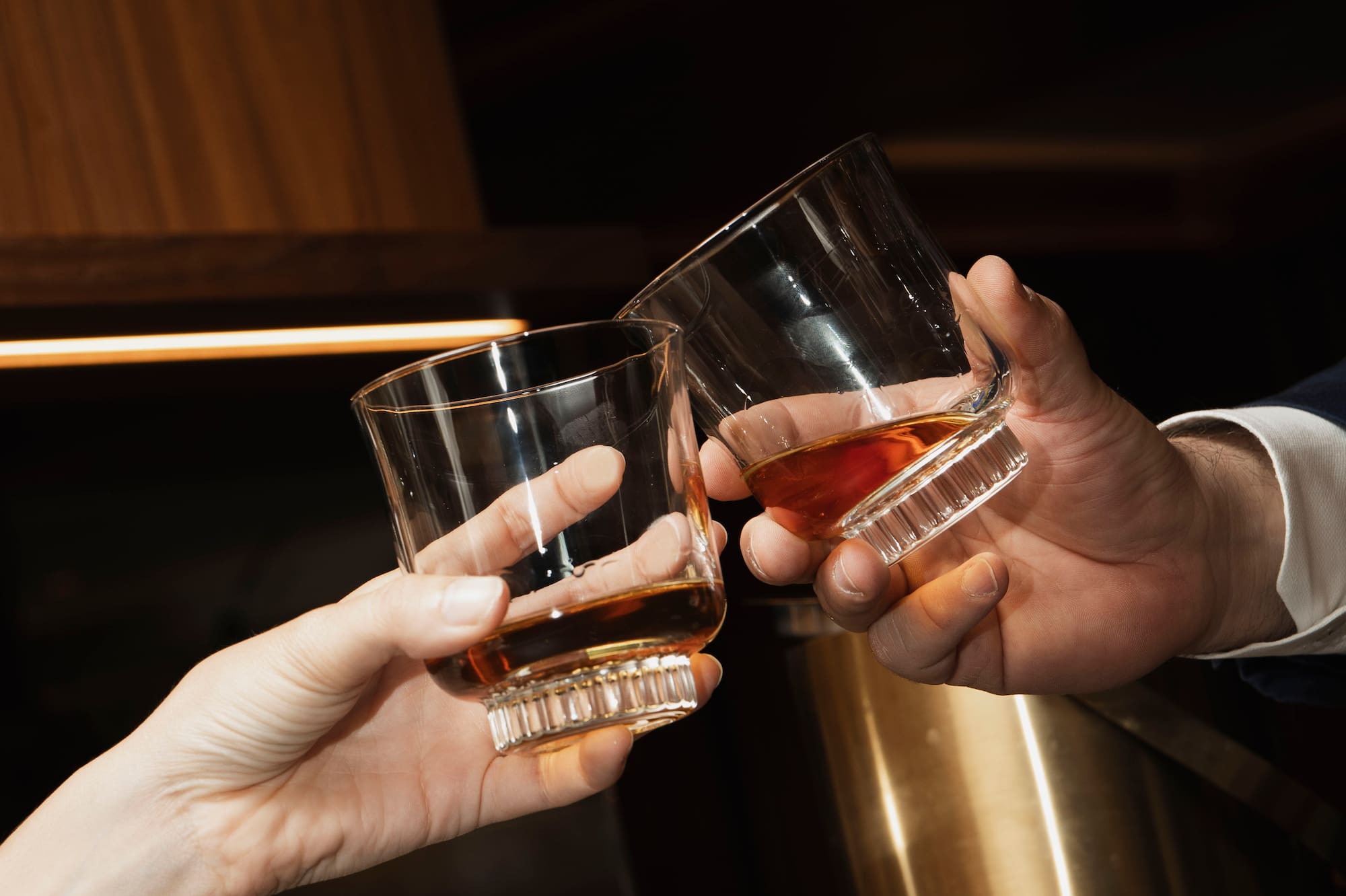 Couple toasting whiskey glasses over a cheese and charcuterie board.