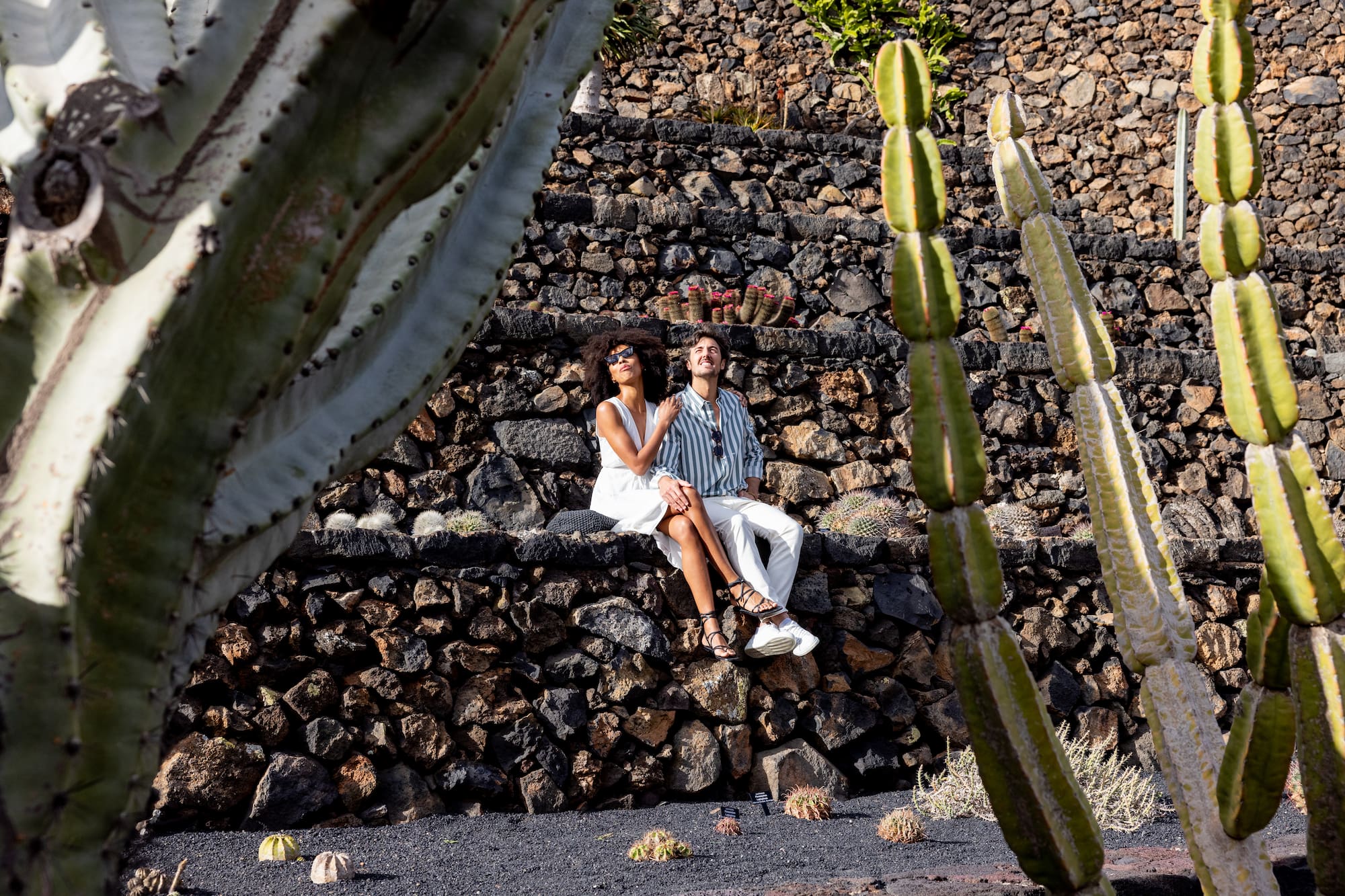 a man and woman sitting on stone steps with cactus