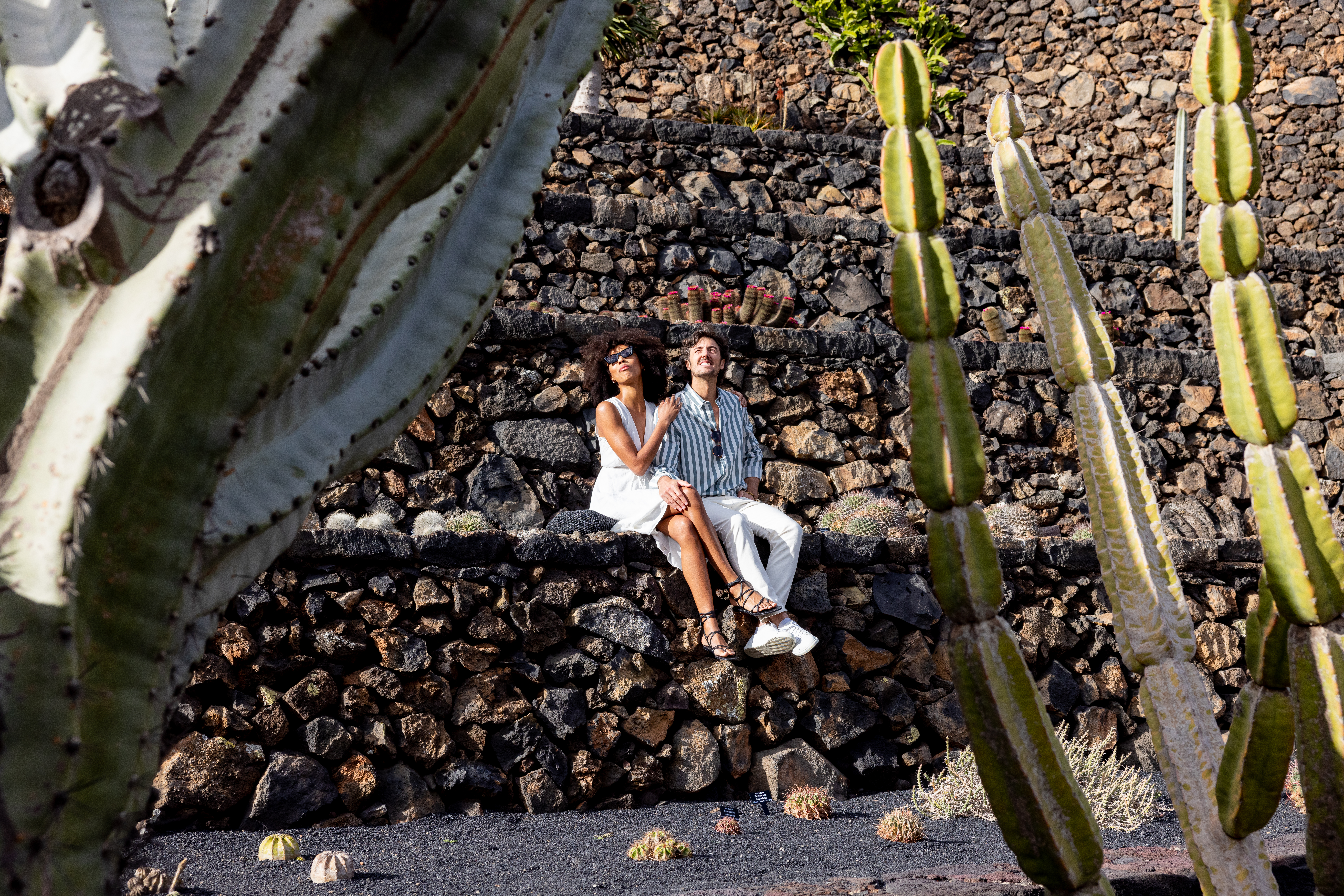 a man and woman sitting on stone steps with cactus