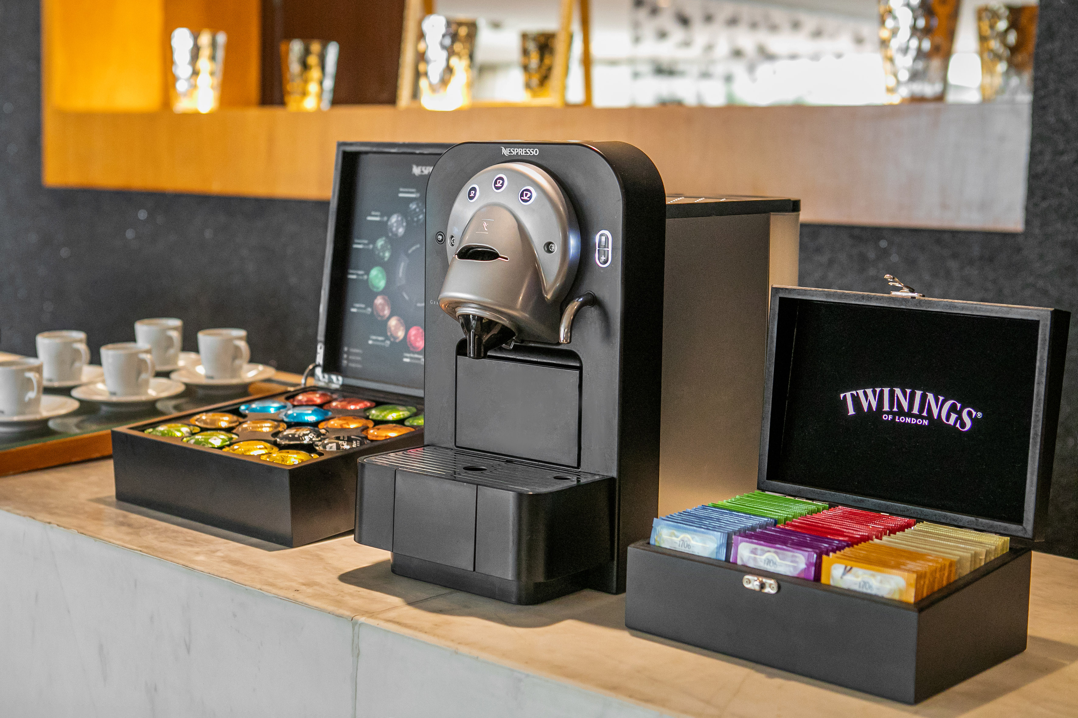 Nespresso coffee maker, colorful capsules, and Twinings tea box on a counter.