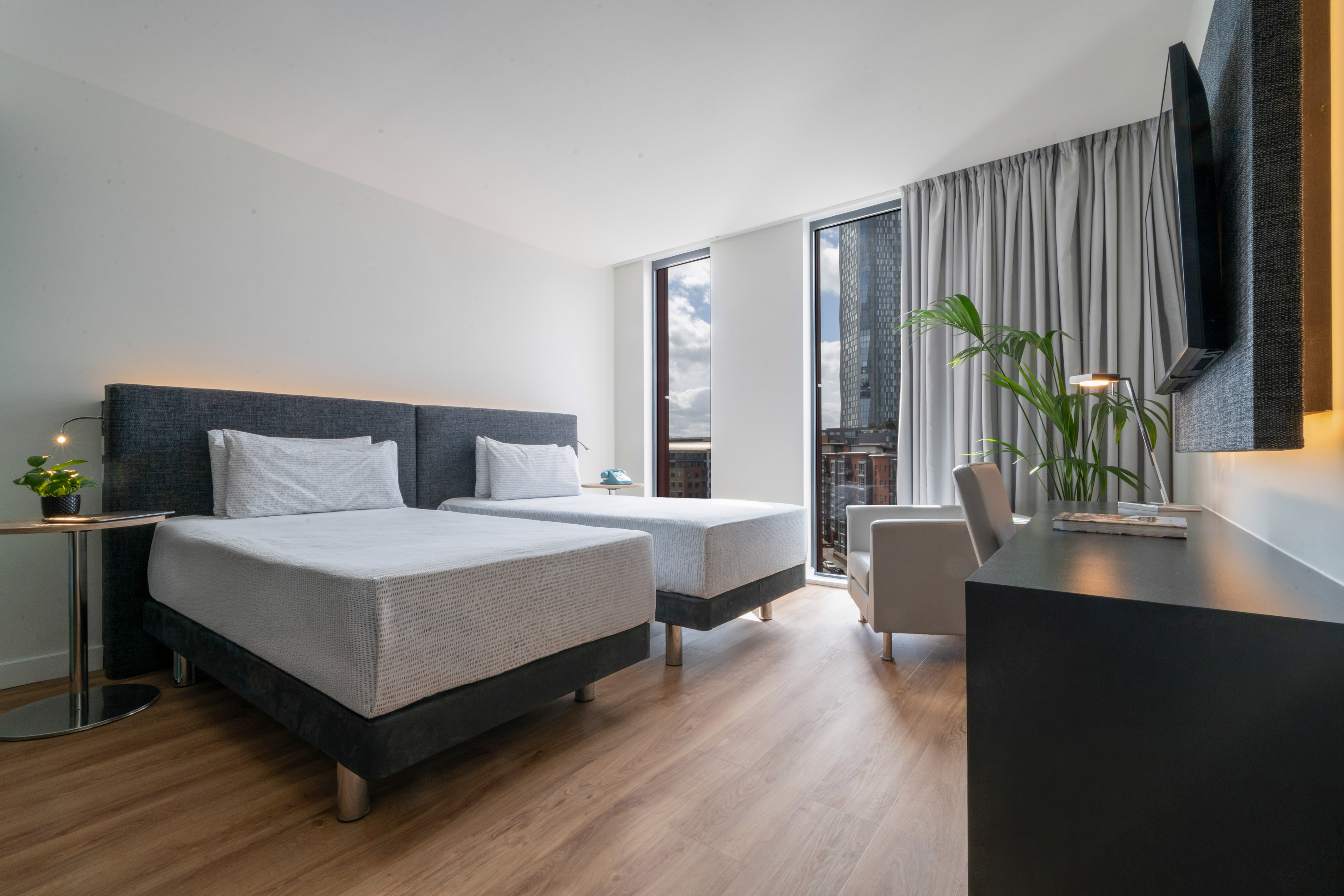 Modern hotel twin room with city view, wooden floor, and work desk.