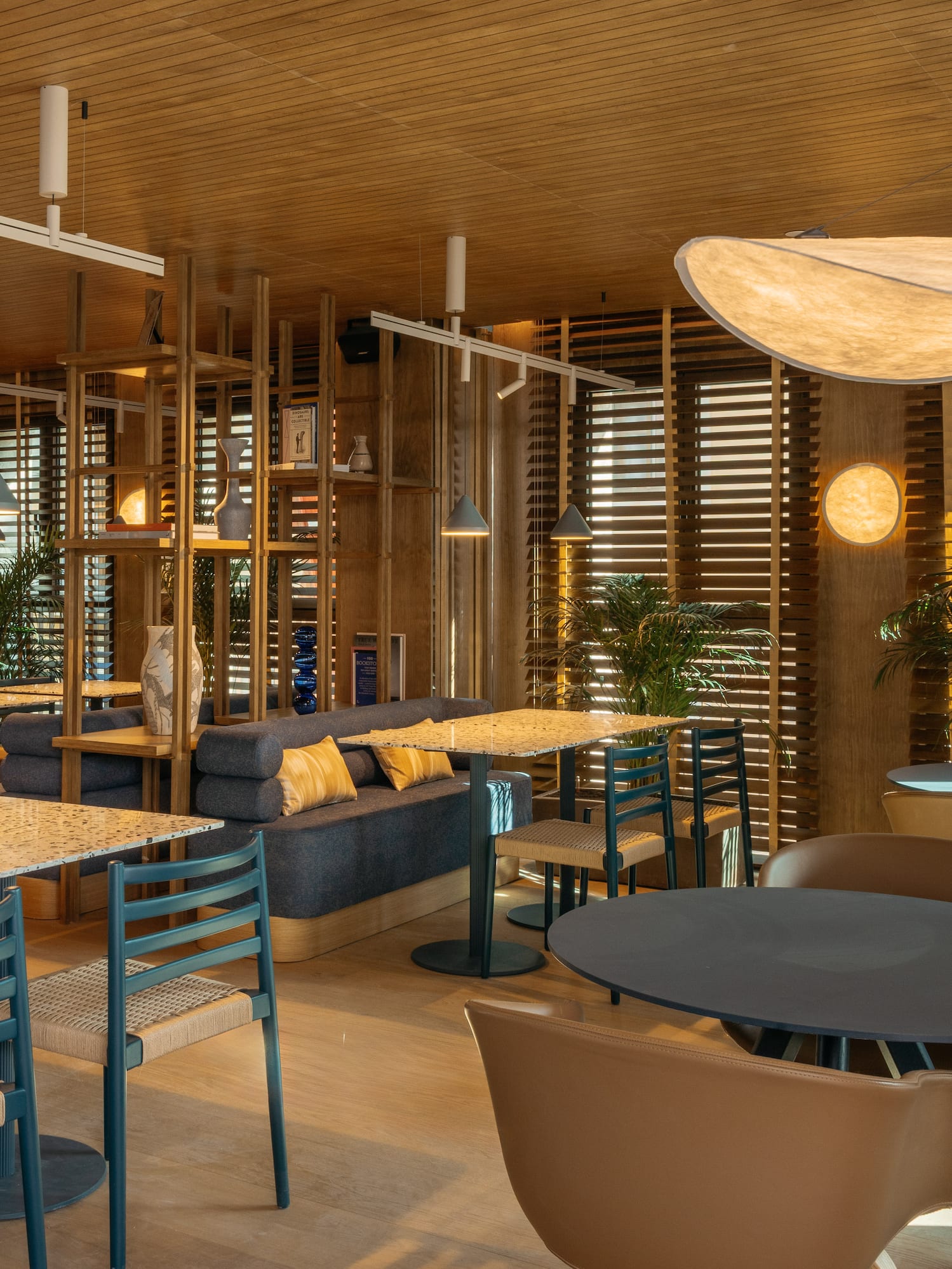 Modern cafe interior with warm wood, diverse seating, plants, and stylish ambient lighting.