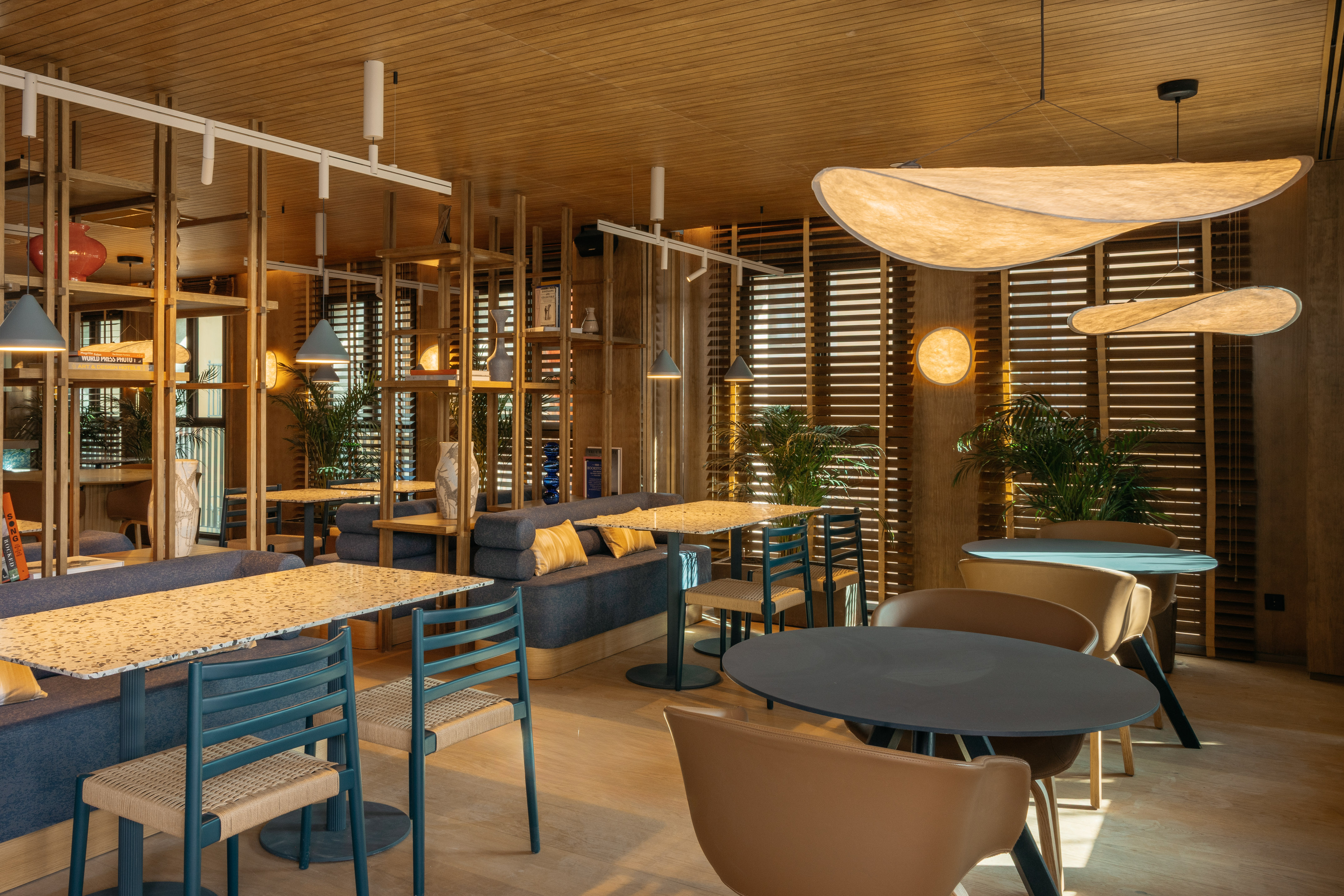 Modern cafe interior with warm wood, diverse seating, plants, and stylish ambient lighting.