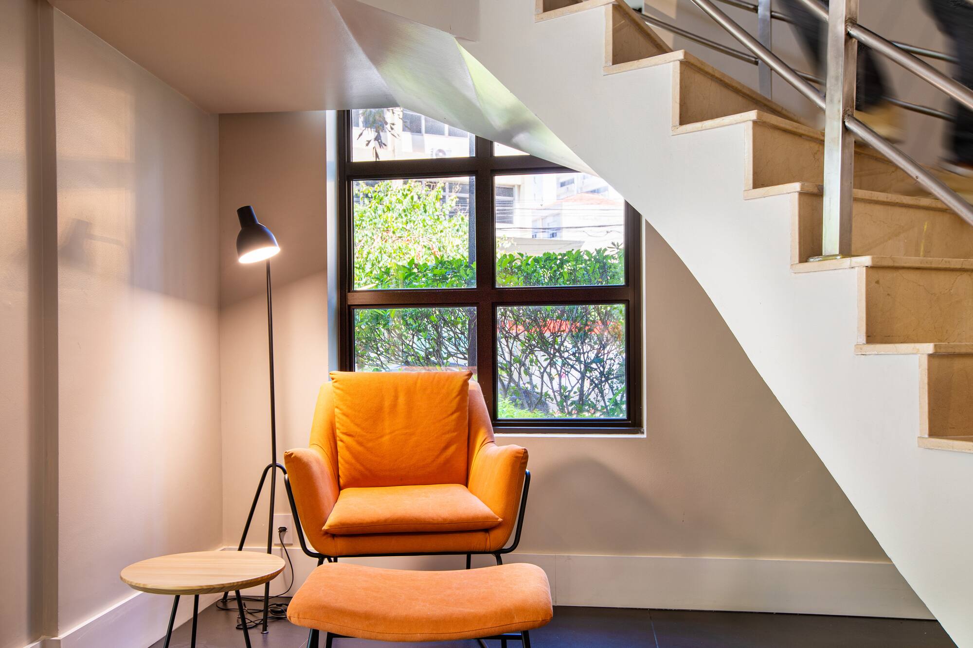 Cozy reading nook with orange armchair, lamp, side table, and staircase.