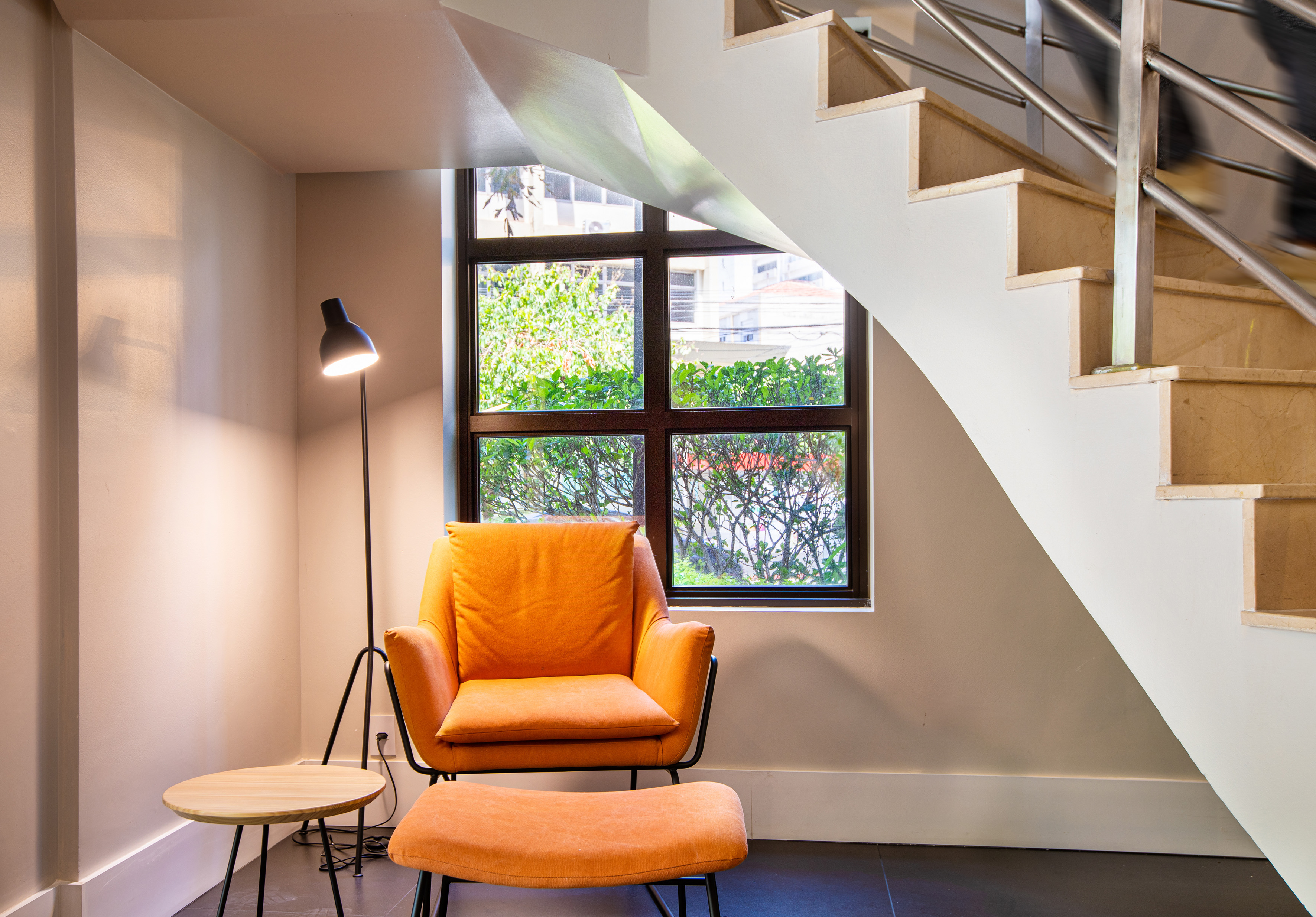 Cozy reading nook with orange armchair, lamp, side table, and staircase.