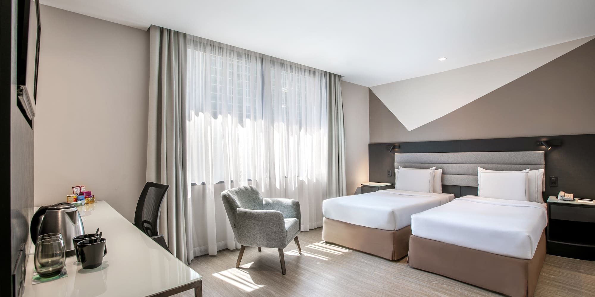 Modern hotel room with twin beds, work desk, and bright window.