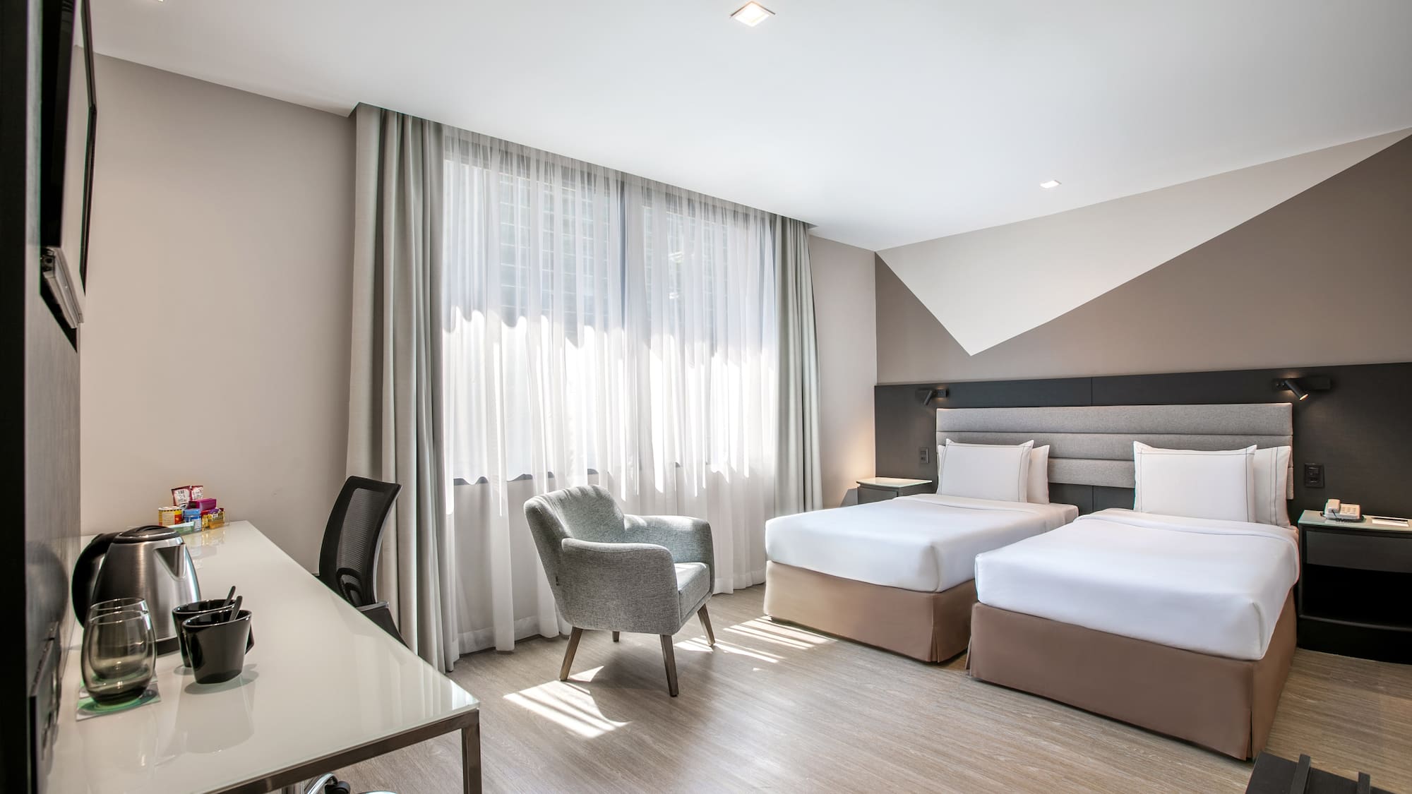 Modern hotel room with twin beds, work desk, and bright window.