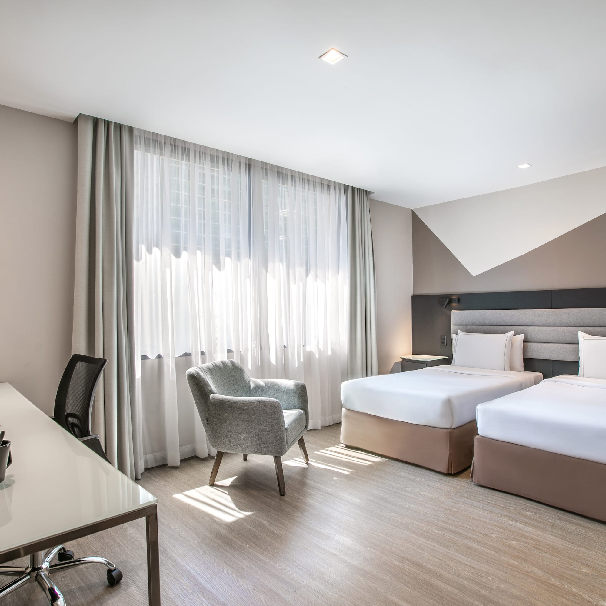 Modern hotel room with twin beds, work desk, and bright window.