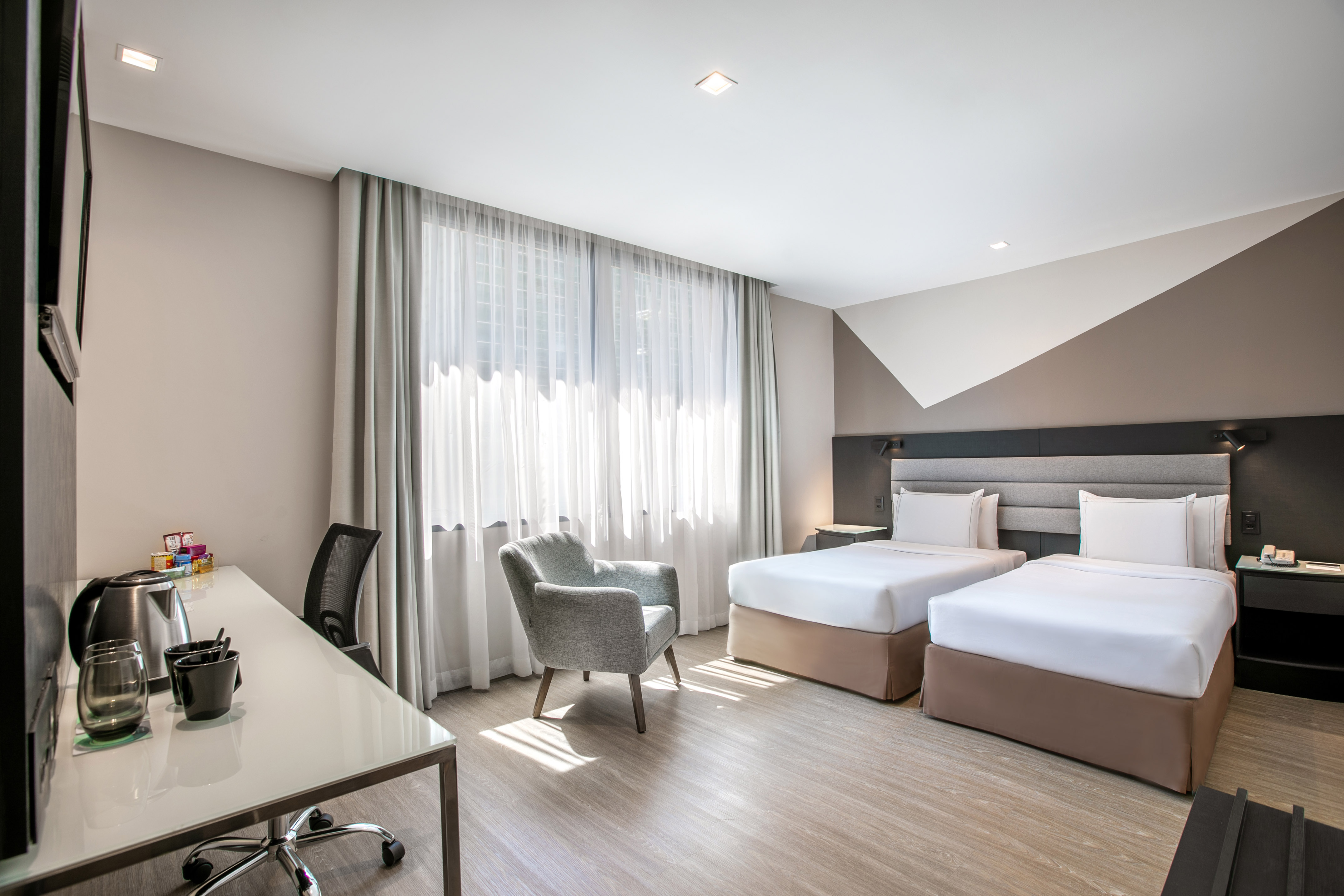 Modern hotel room with twin beds, work desk, and bright window.