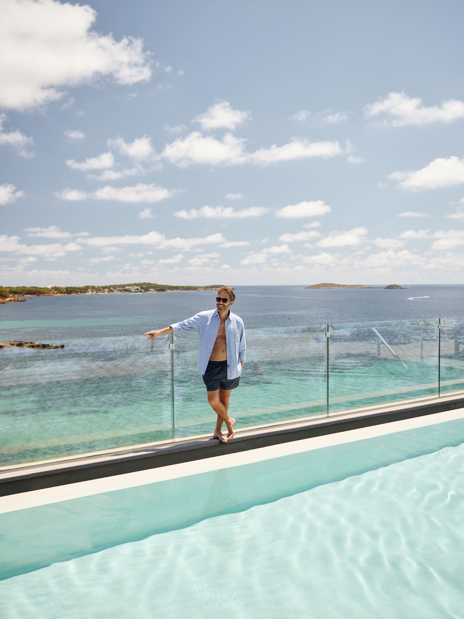 a man standing on a ledge of a pool with a body of water in the background