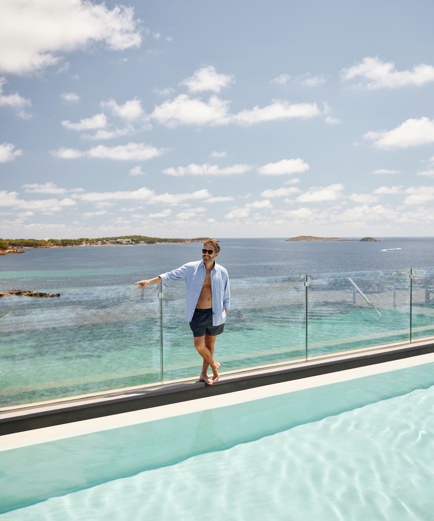 a man standing on a ledge of a pool with a body of water in the background