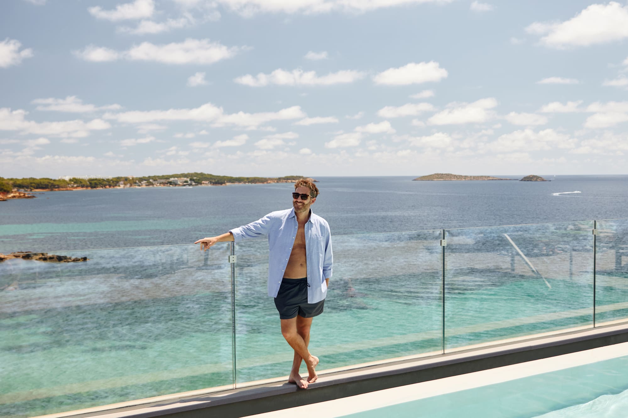a man standing on a ledge of a pool with a body of water in the background