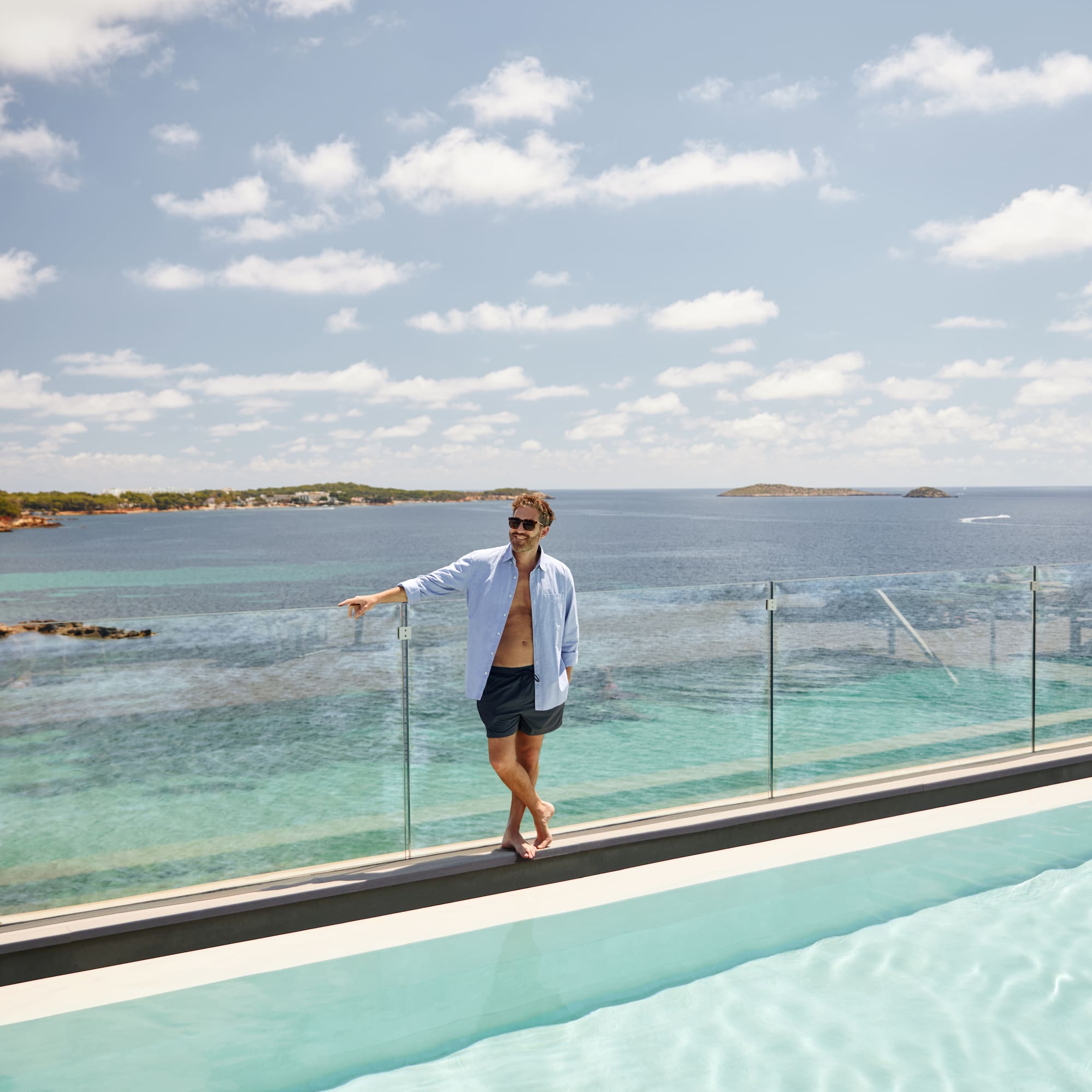 a man standing on a ledge of a pool with a body of water in the background