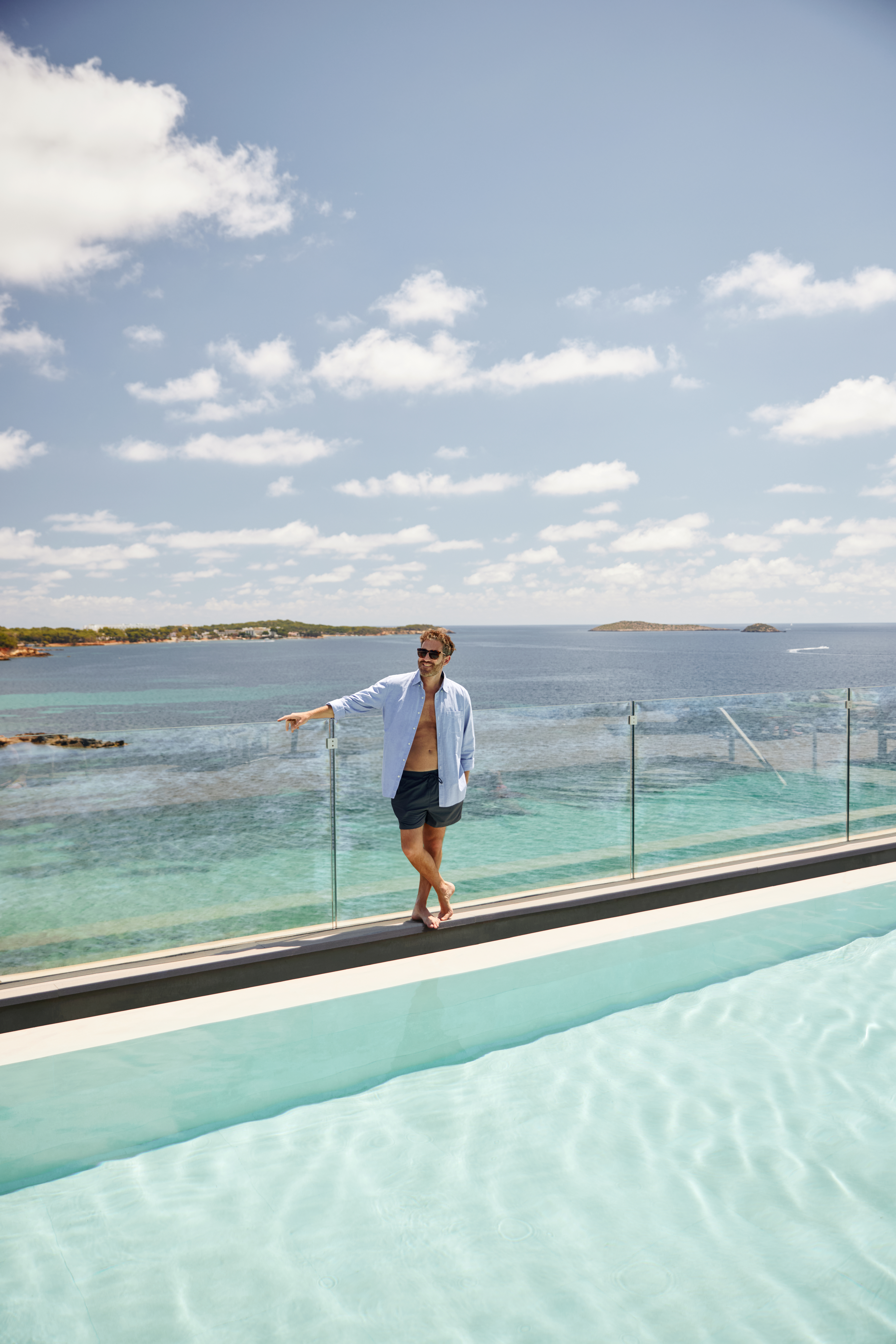 a man standing on a ledge of a pool with a body of water in the background