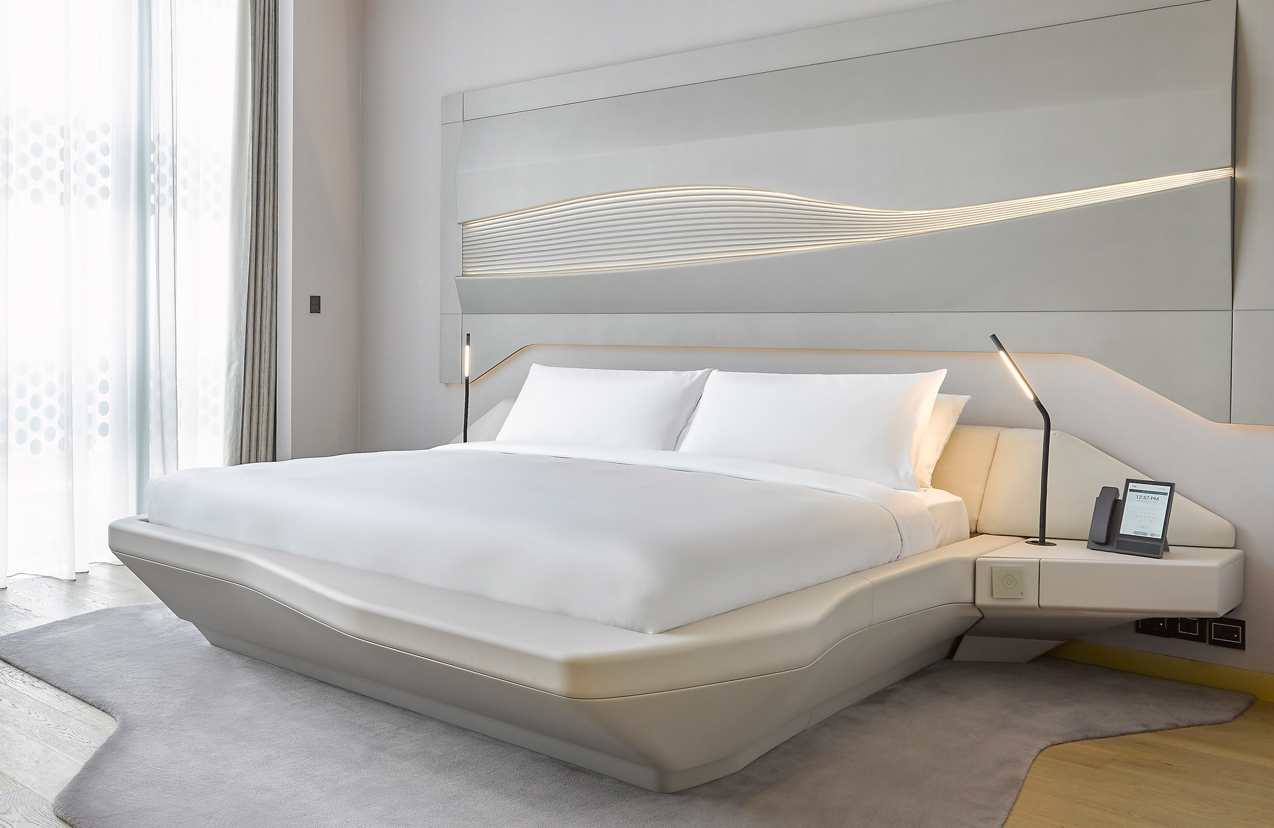 Contemporary hotel bed with white linens, illuminated headboard, integrated nightstand.