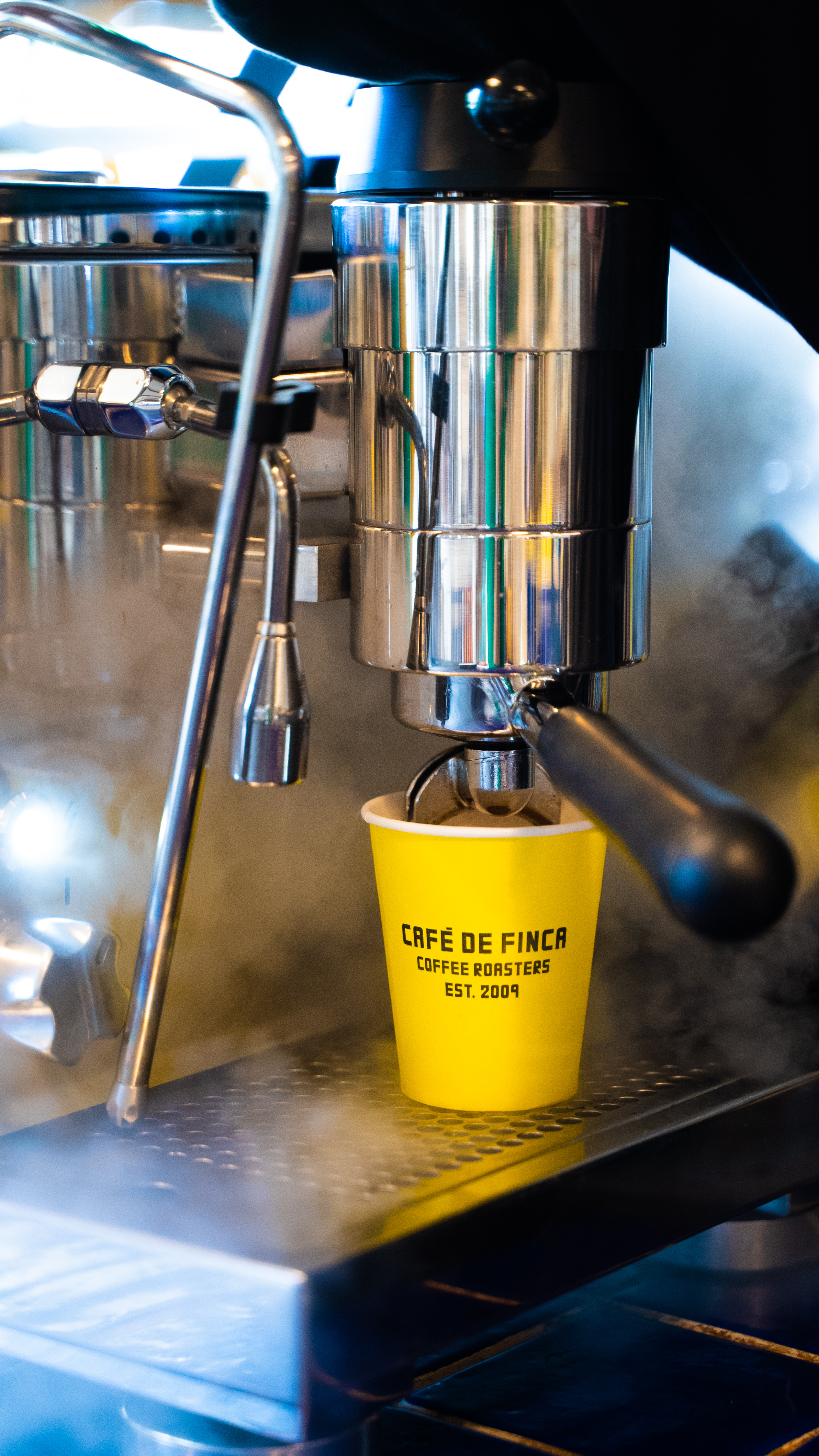 Steaming espresso machine brewing into a yellow Café de Finca coffee cup.