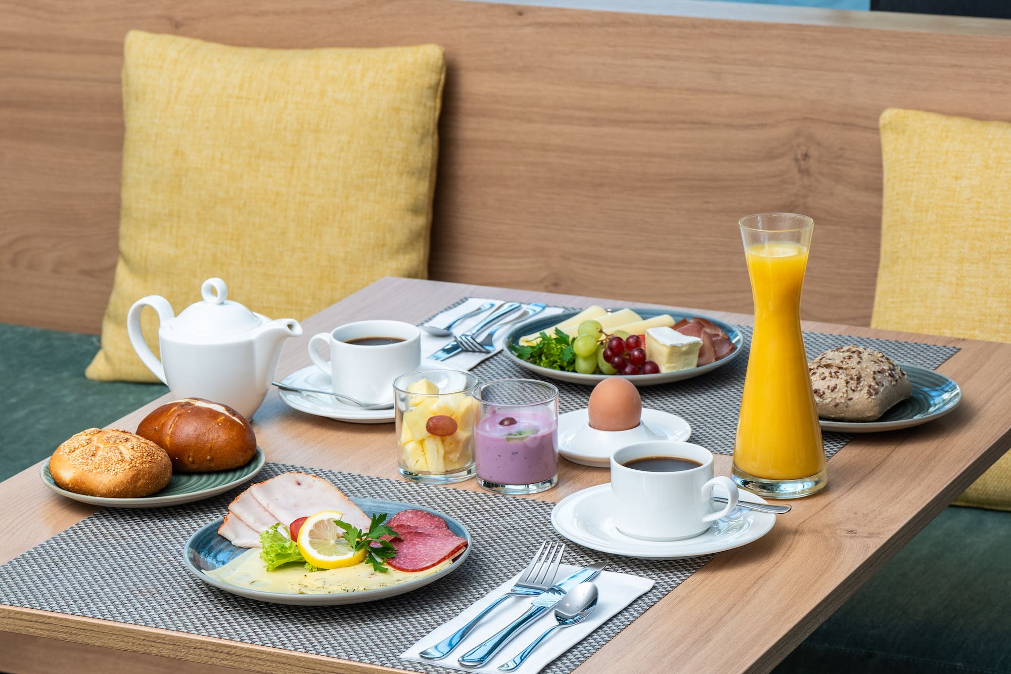 Diverse hotel breakfast with coffee, juice, rolls, cheese, cold cuts & fruit.
