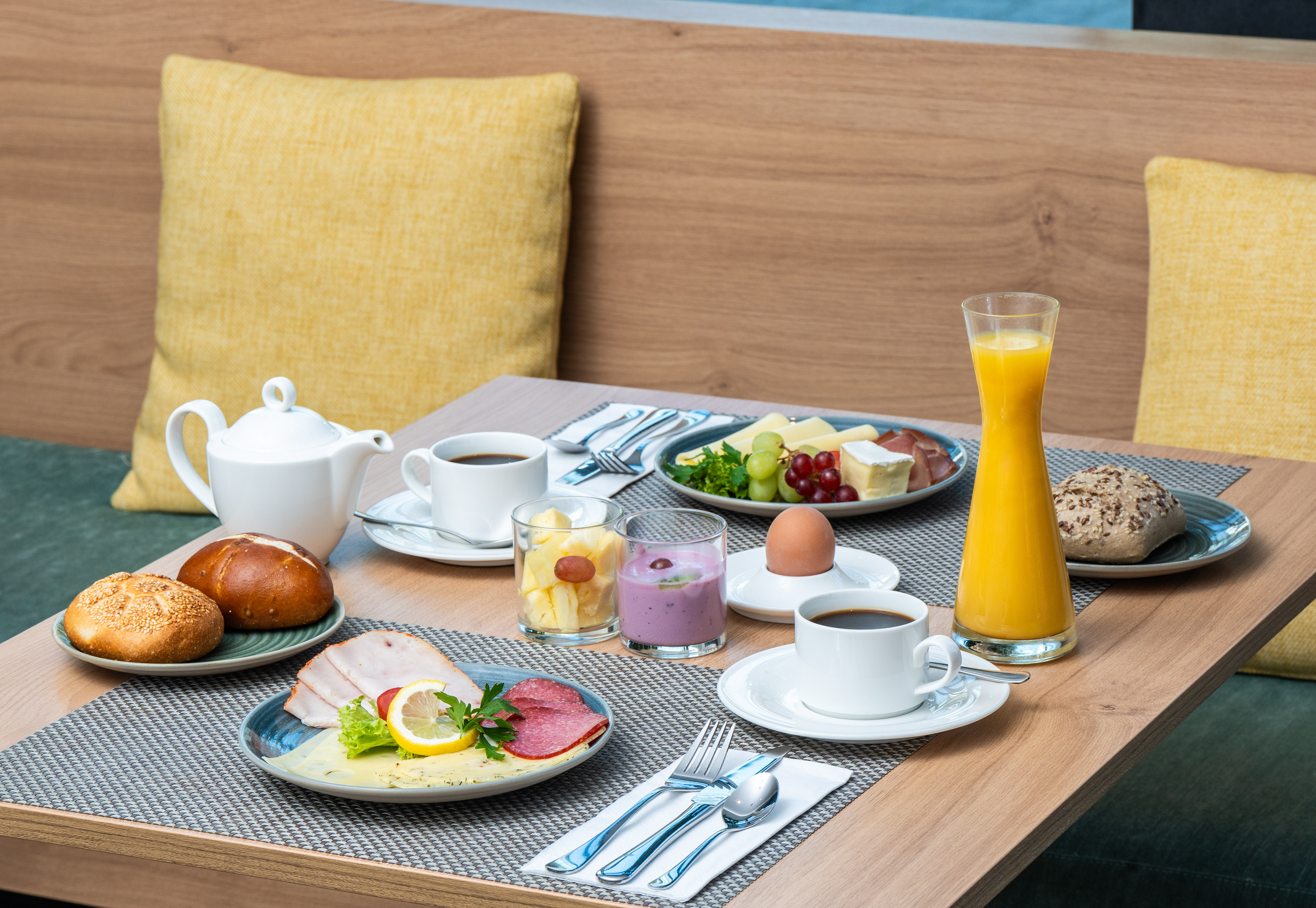Diverse hotel breakfast with coffee, juice, rolls, cheese, cold cuts & fruit.