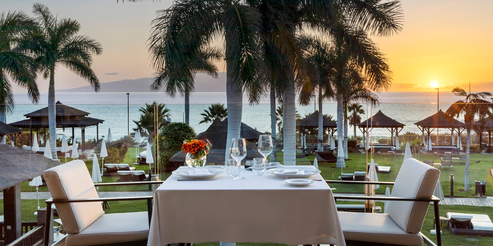 a table with plates and flowers on it and chairs on a deck overlooking a beach
