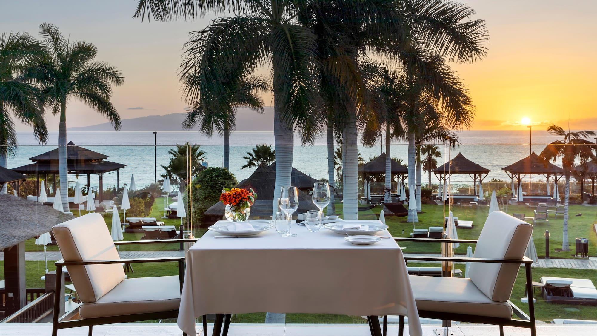 a table with plates and flowers on it and chairs on a deck overlooking a beach