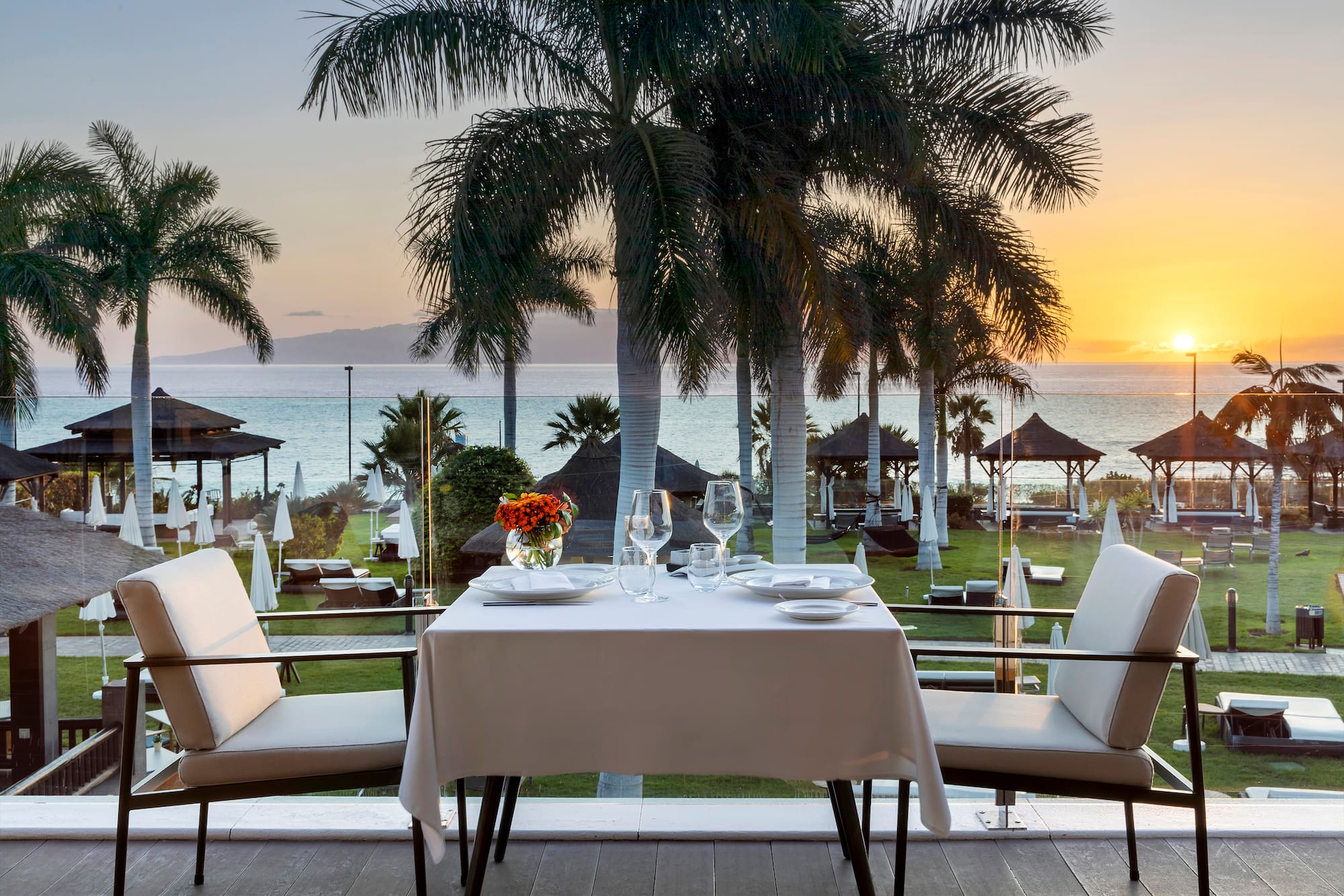 a table with plates and flowers on it and chairs on a deck overlooking a beach