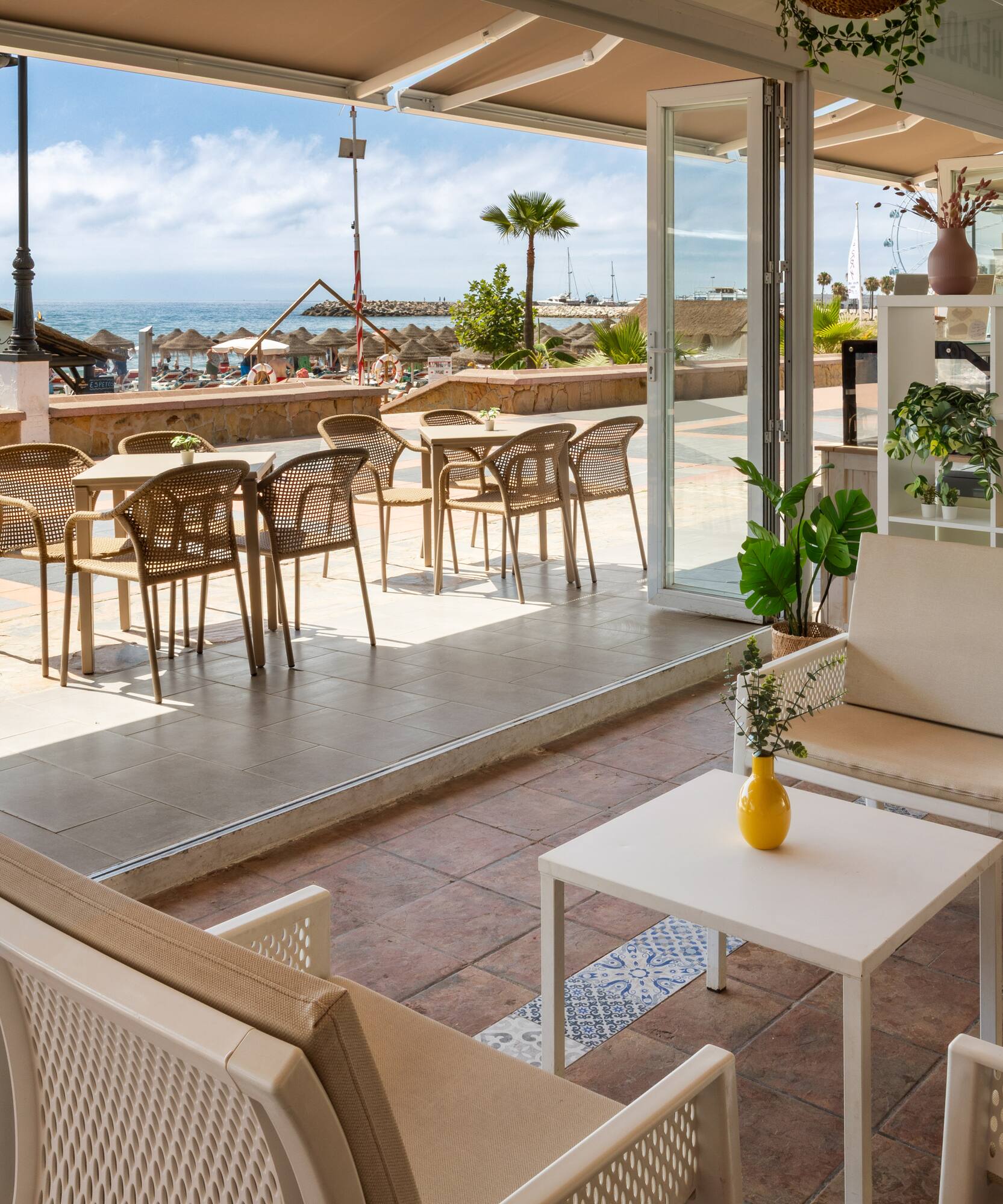 Terraza de chiringuito en la playa con mesas, sillas y vista al mar.