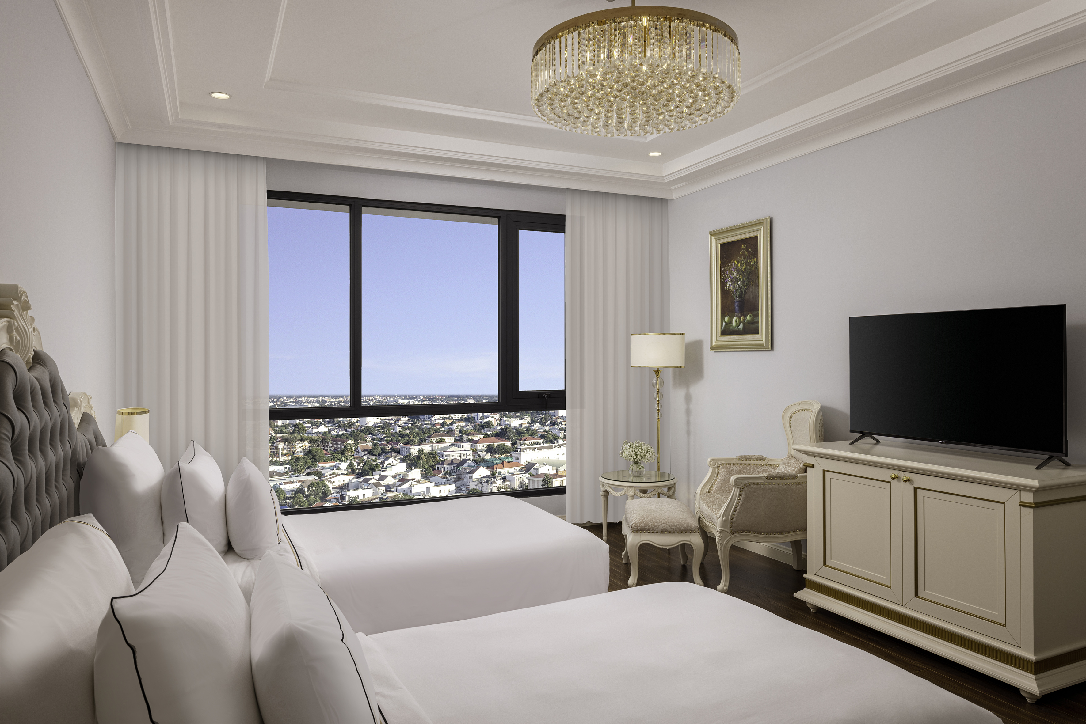 Elegant hotel room with twin beds, large window city view, chandelier, and TV.