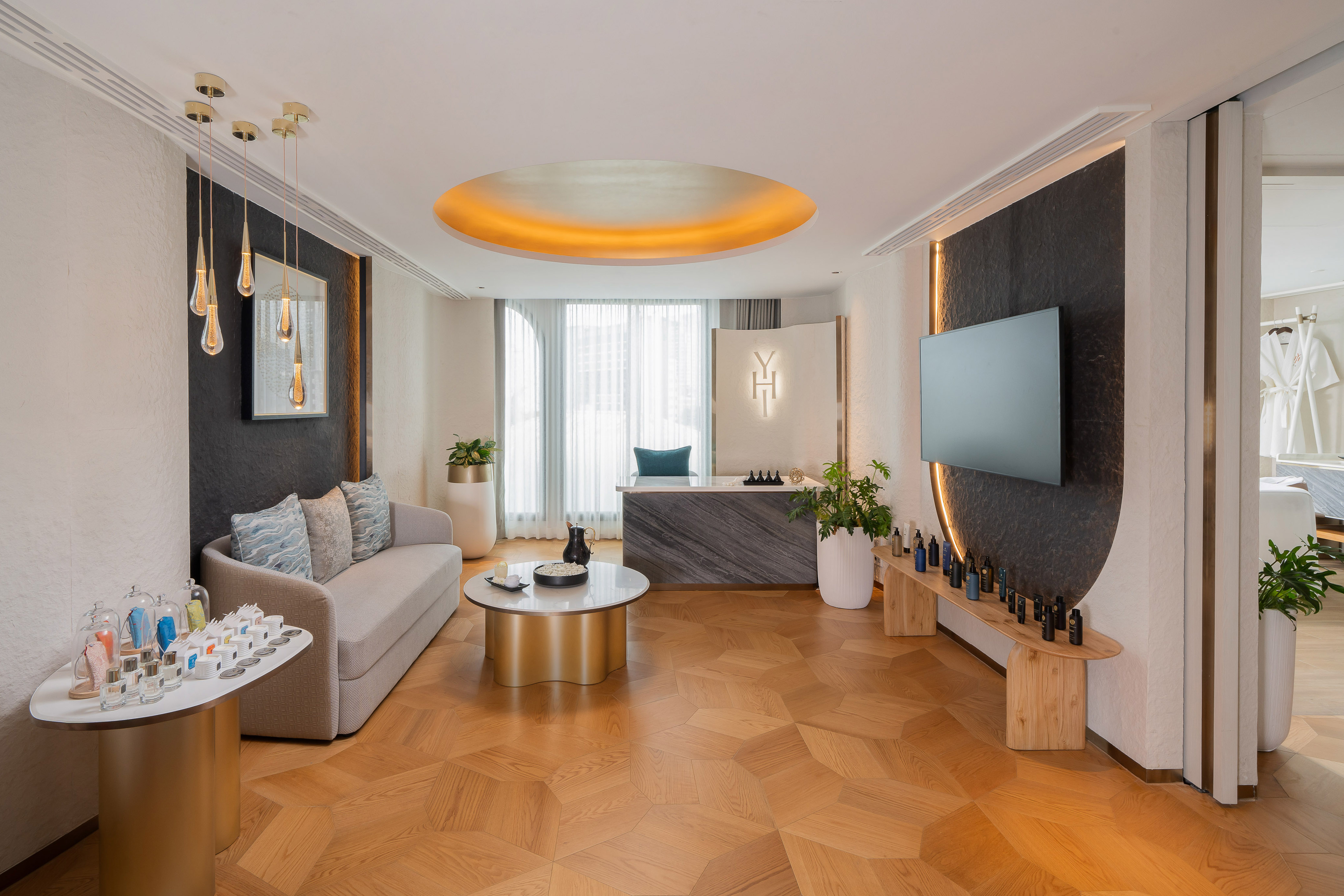 Modern luxury spa reception with geometric wood floor, comfy sofa, and product display.