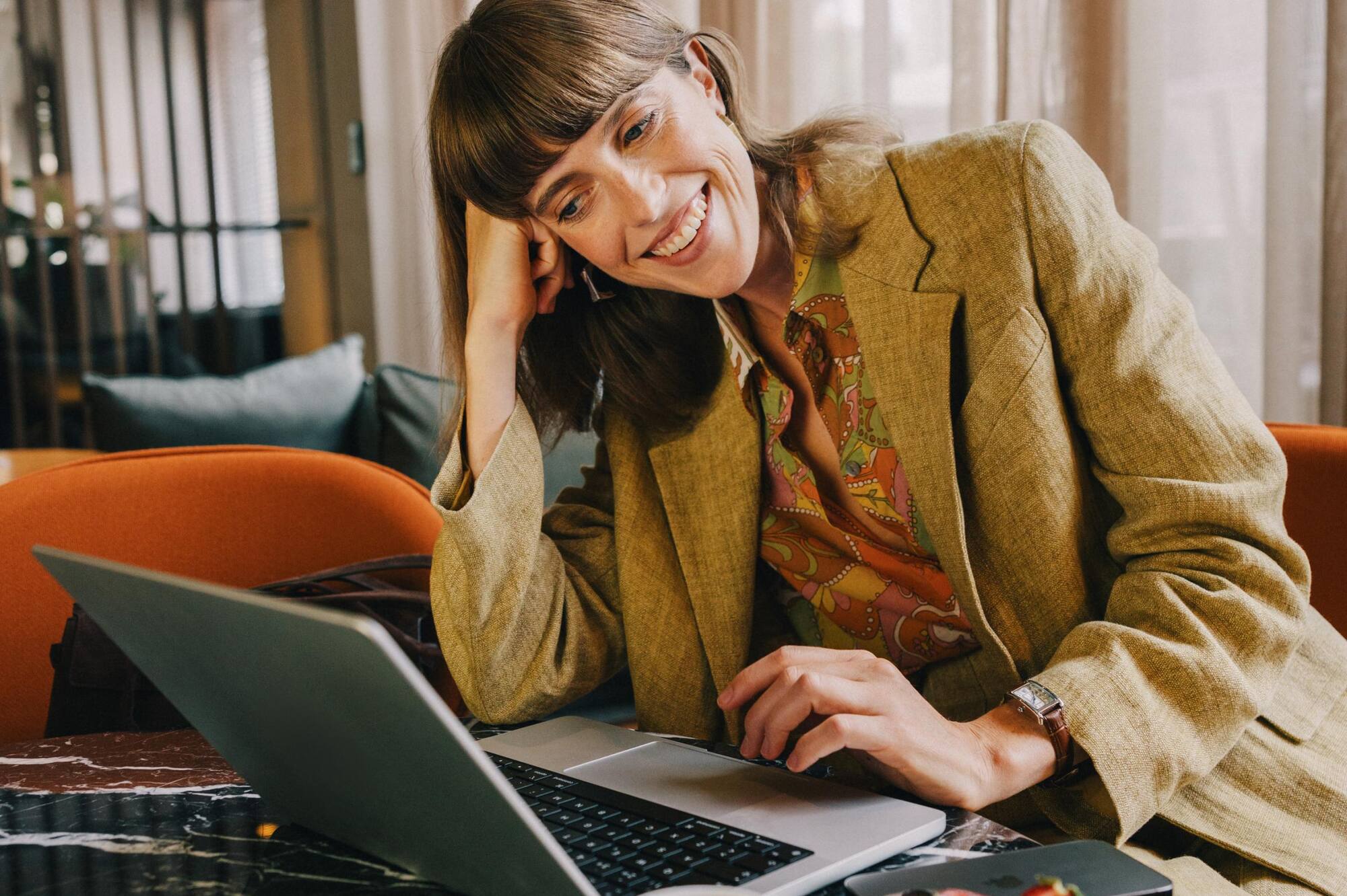 Smiling woman working on laptop at cafe table with coffee and berry tart.