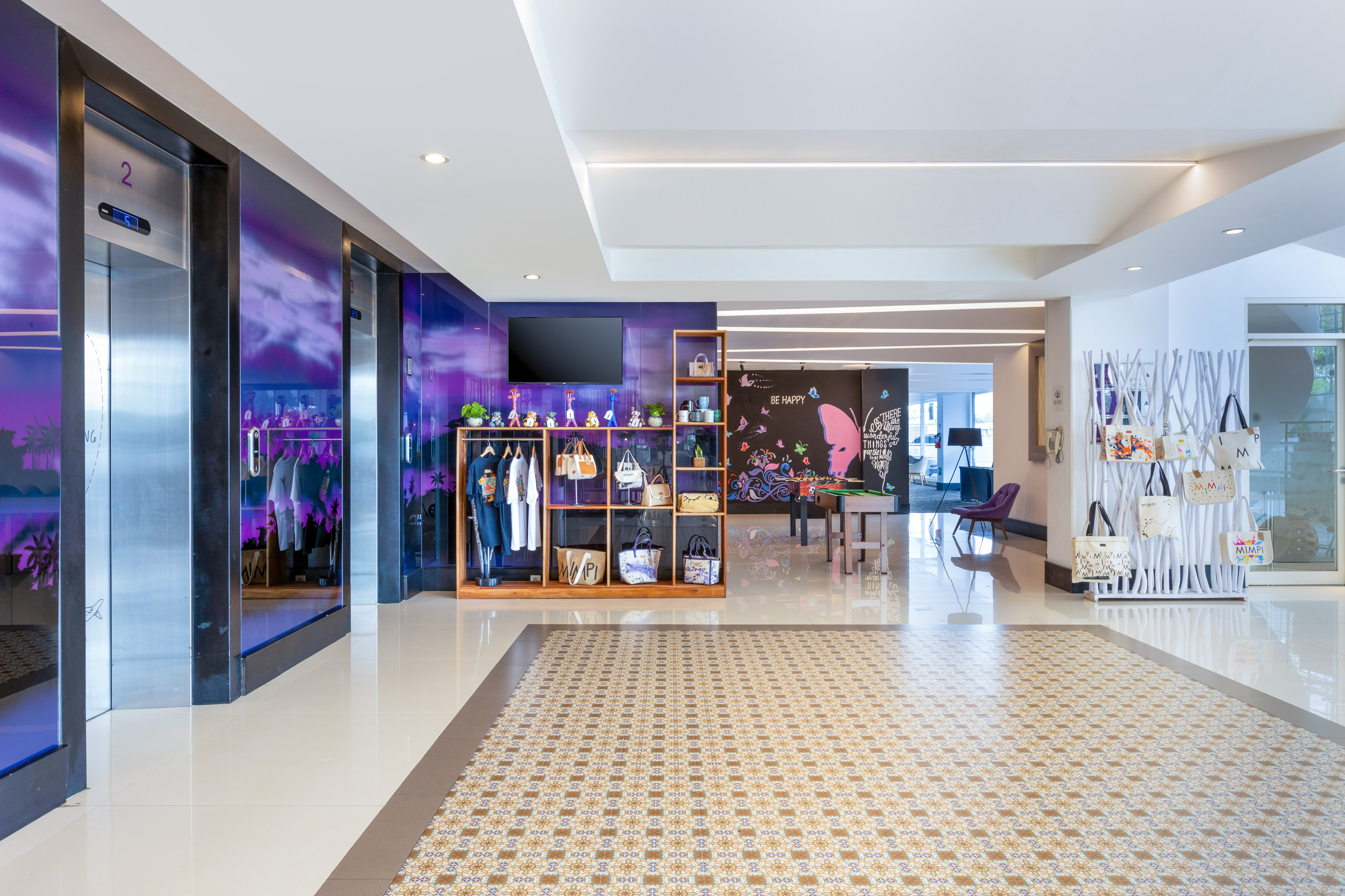 Modern hotel lobby with purple elevators, retail merchandise, and patterned floor.