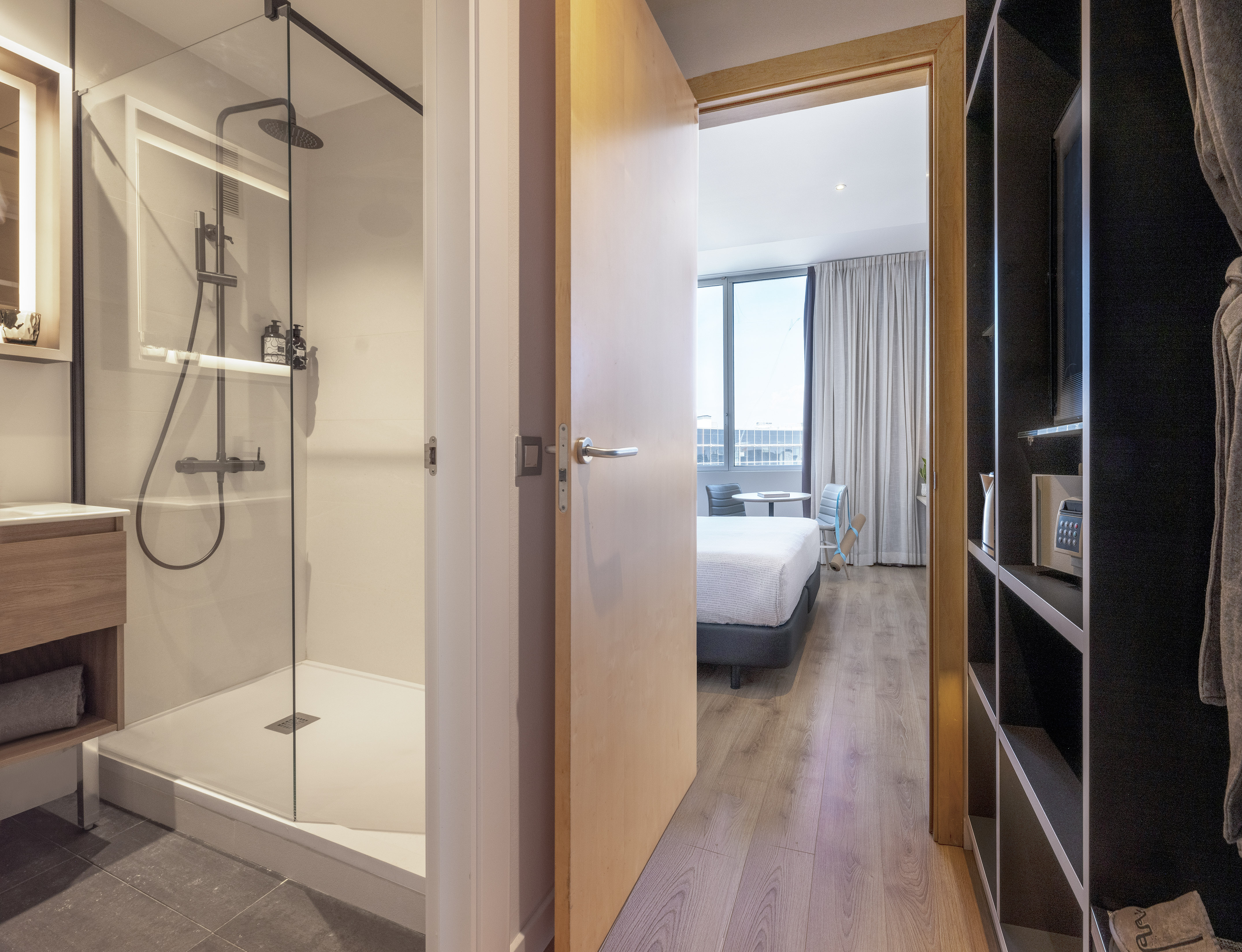 Modern hotel room with ensuite walk-in shower, bedroom, and wardrobe.