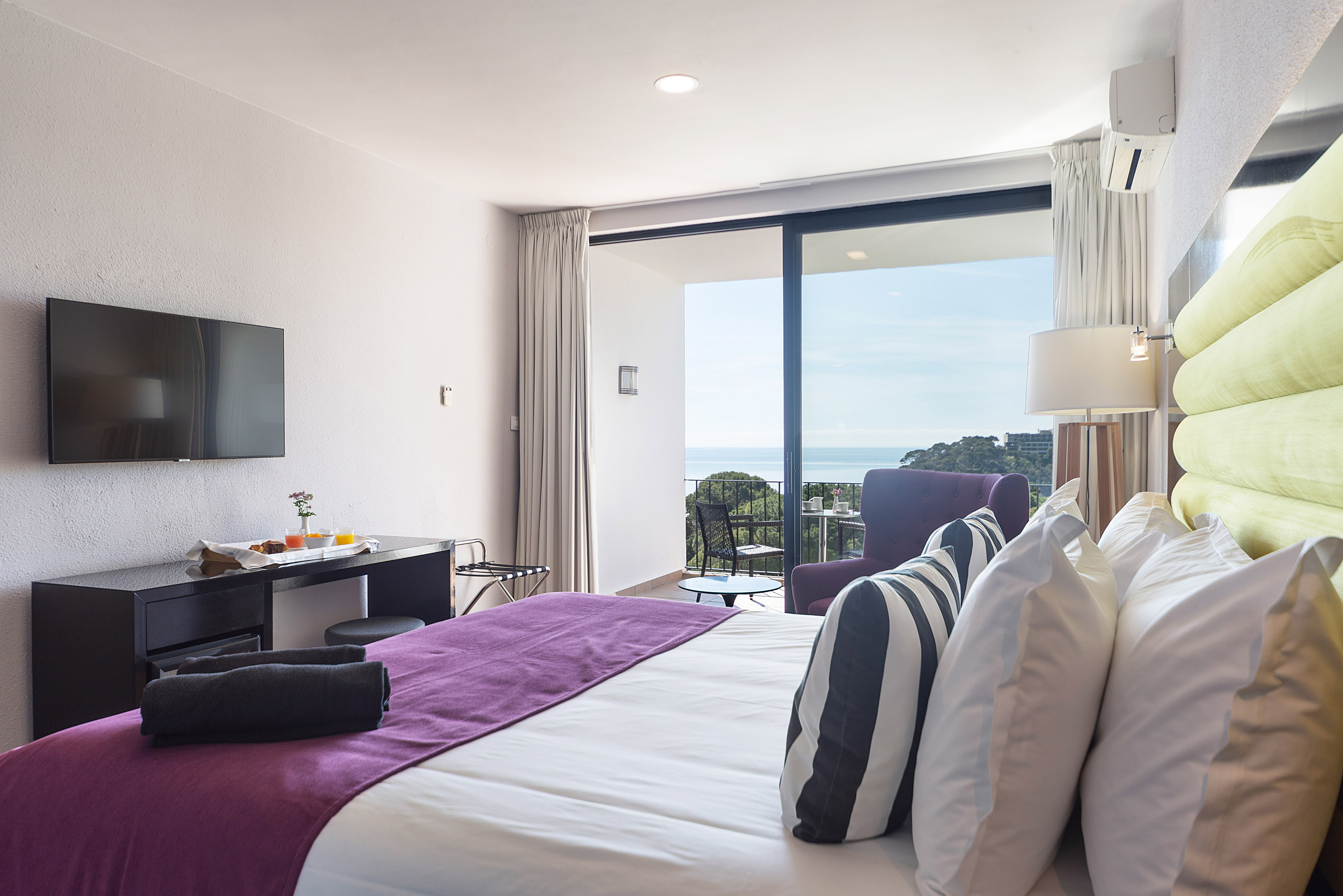Modern hotel room with bed, TV, and balcony offering a beautiful sea view.