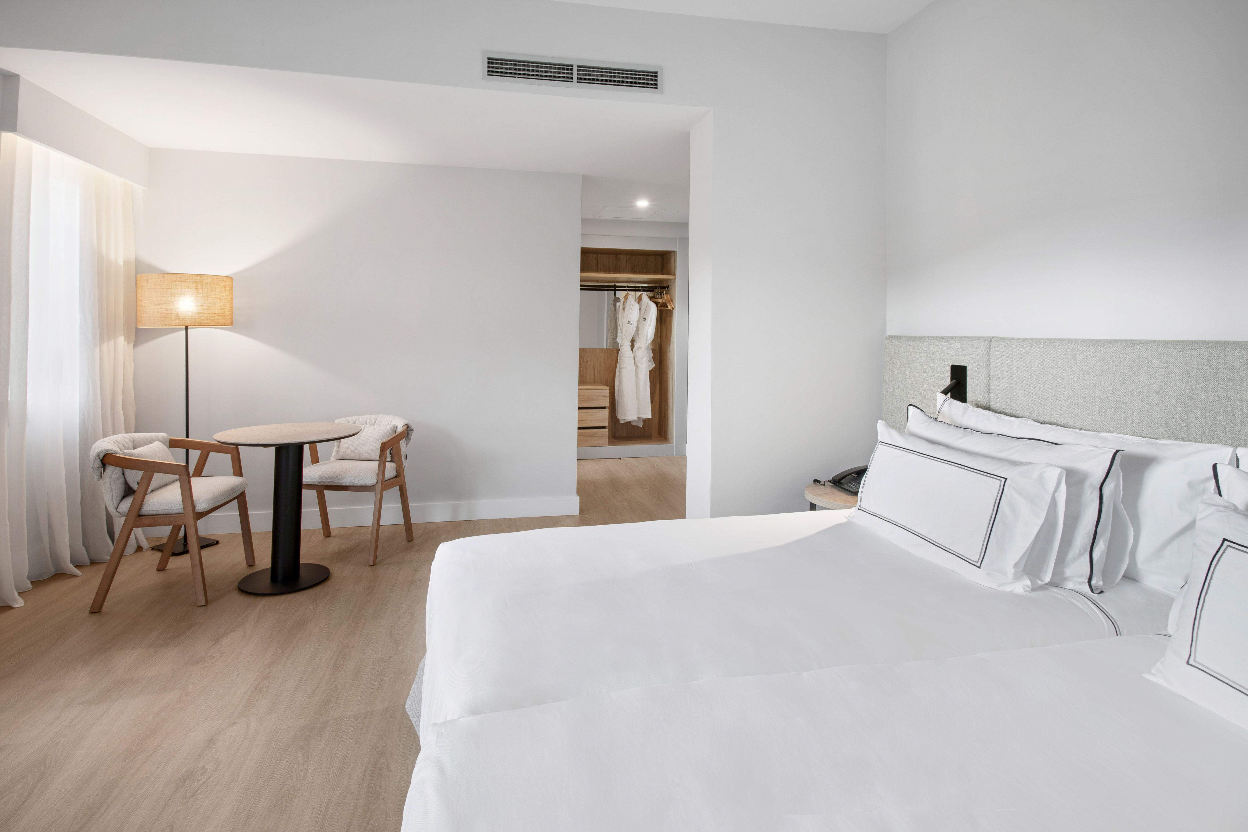 Bright modern hotel room with bed, two chairs, table, and open closet.