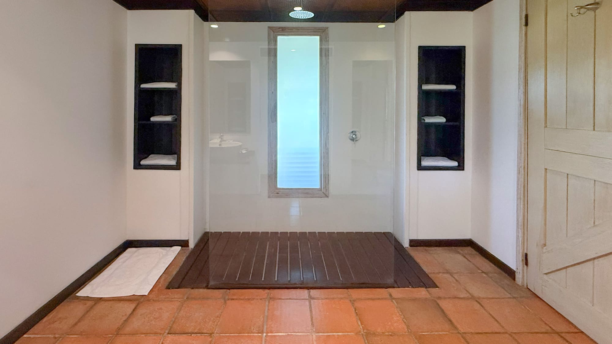 Modern walk-in shower with glass enclosure, rain head, wood floor, terracotta tiles.